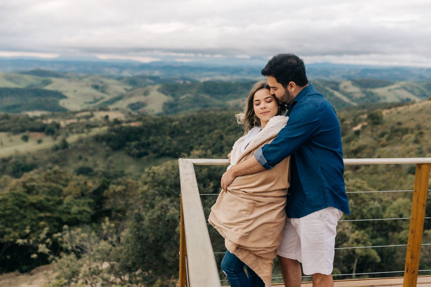 A couple shares an intimate moment on a mountain observation deck with scenic valley views.