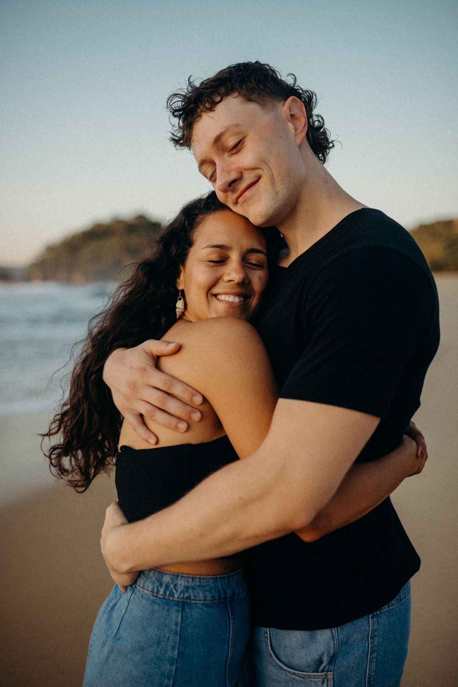 Intimate couple moment captured on sandy beach during golden hour.