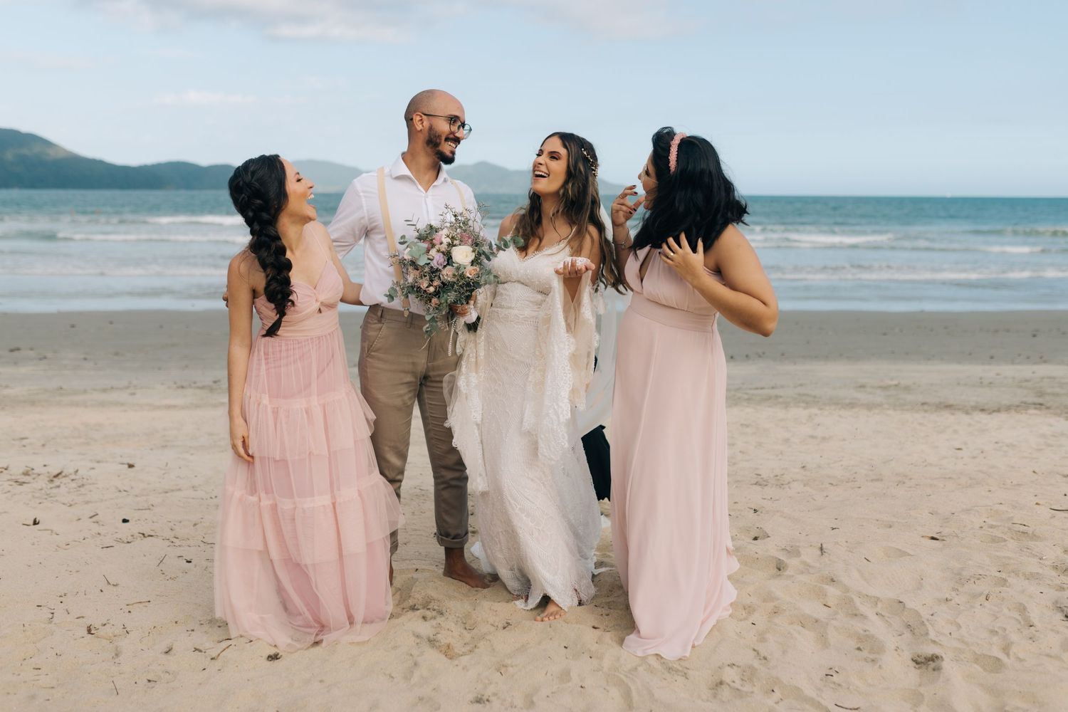 Wedding group photo session with pink dresses and tan suits on a tropical beach.