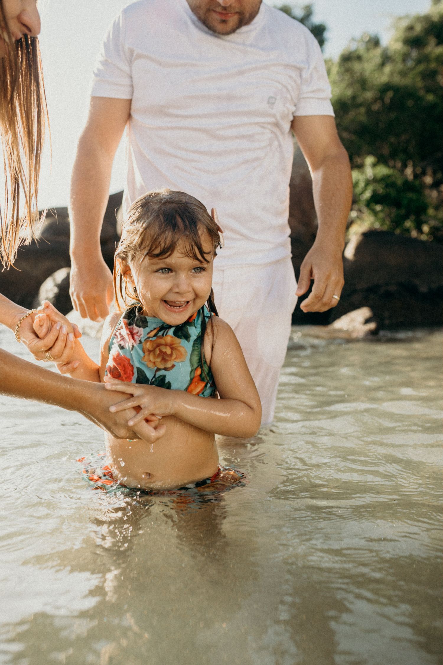 Child splashing and playing in ocean waves while holding hands with adults.