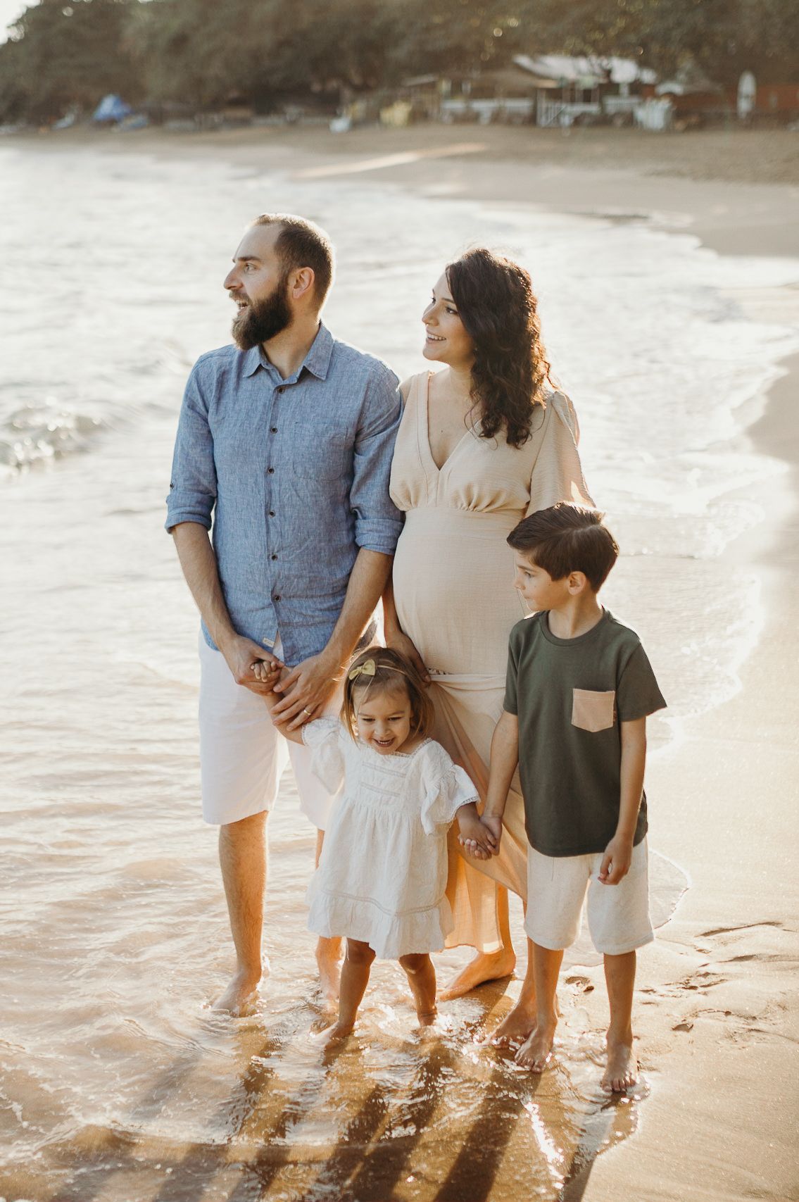 Family of four poses together on a sunlit beach during golden hour.