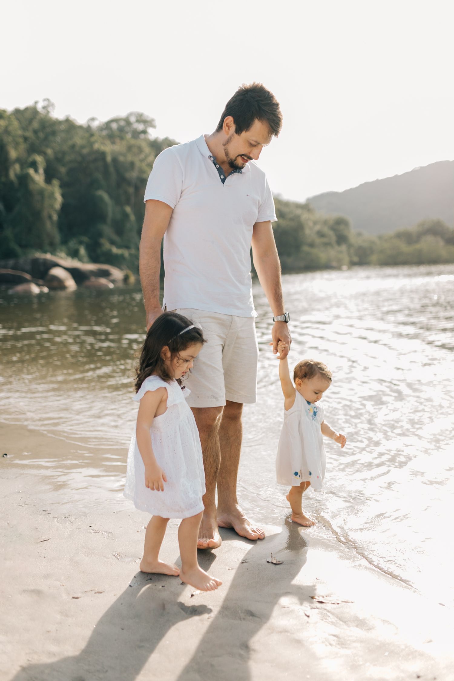 Three people walk along the shoreline in white clothing during a peaceful beach day.