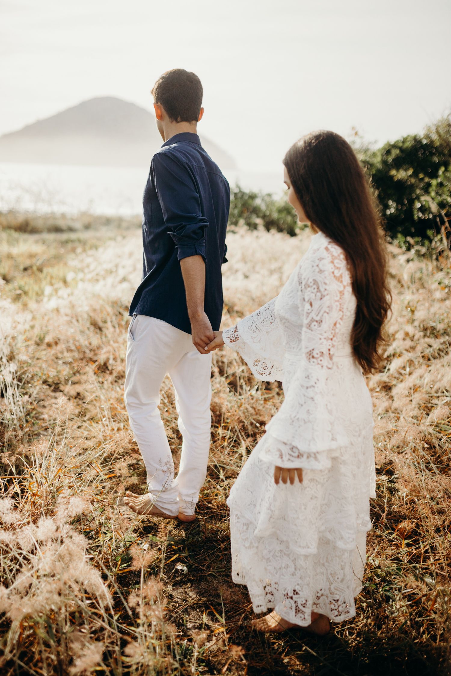 Two people walking through tall grass wearing white and navy blue outfits against a nature backdrop.