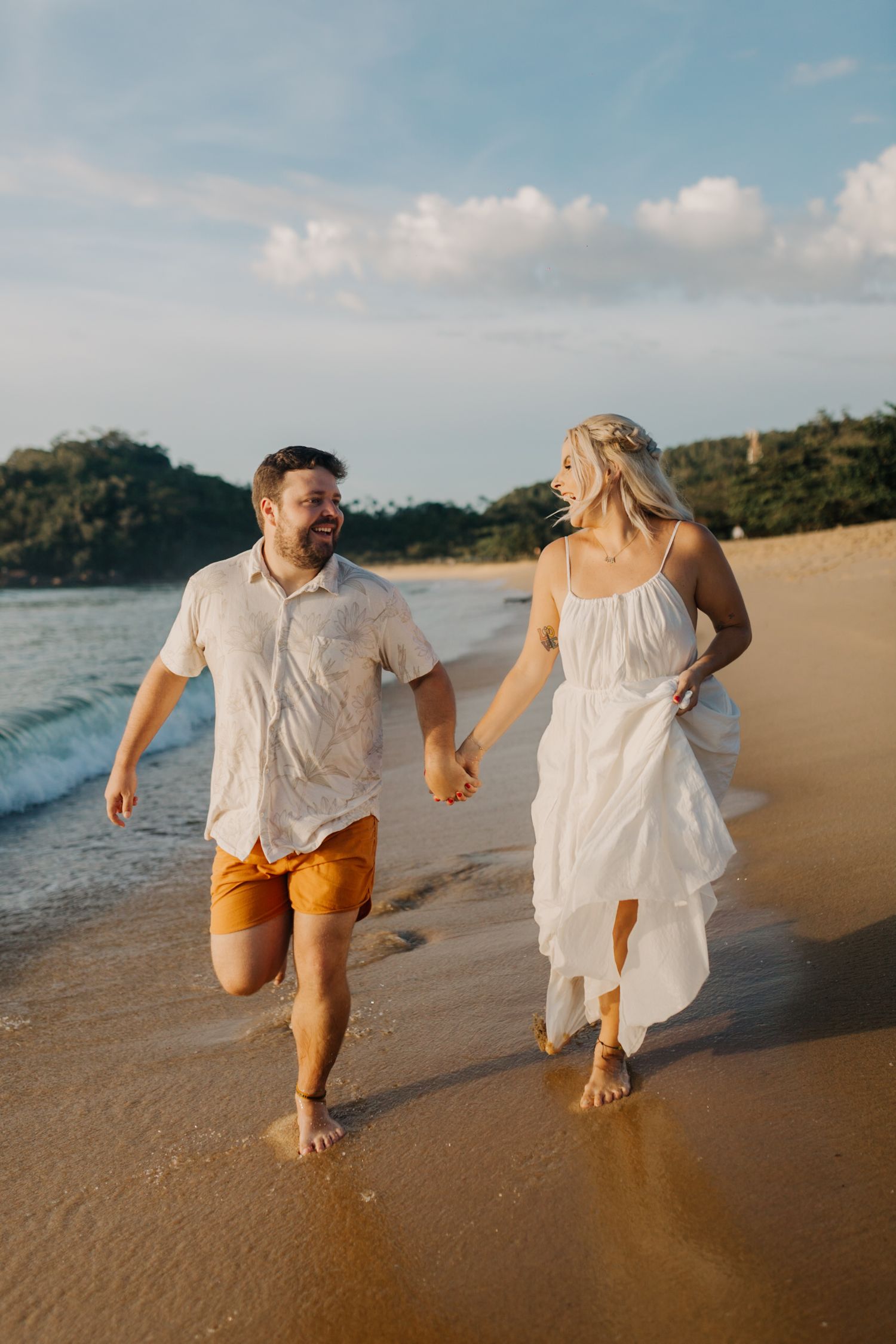 Couple laughing while walking together on scenic beach with waves rolling in.