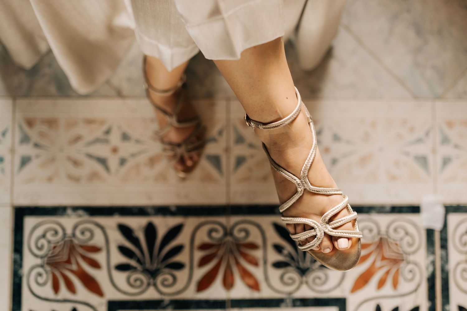 Detail shot of elegant strappy heels on ornate decorative floor tiles.