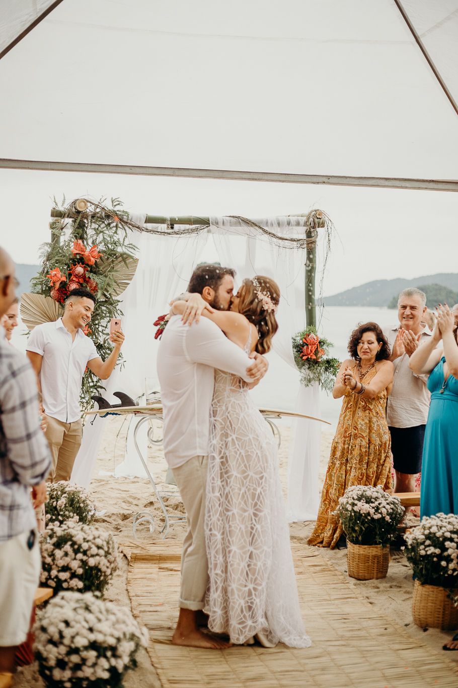 Wedding party members celebrate with dancing under a white tent by the ocean.