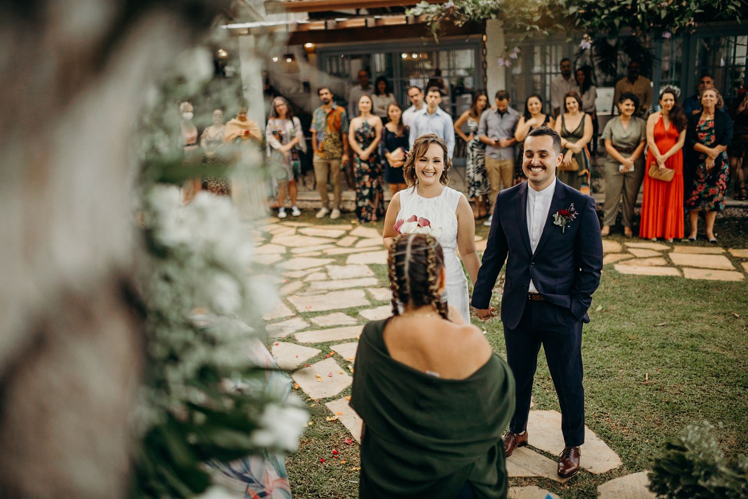 Wedding guests gather on a lawn during an outdoor daytime ceremony.