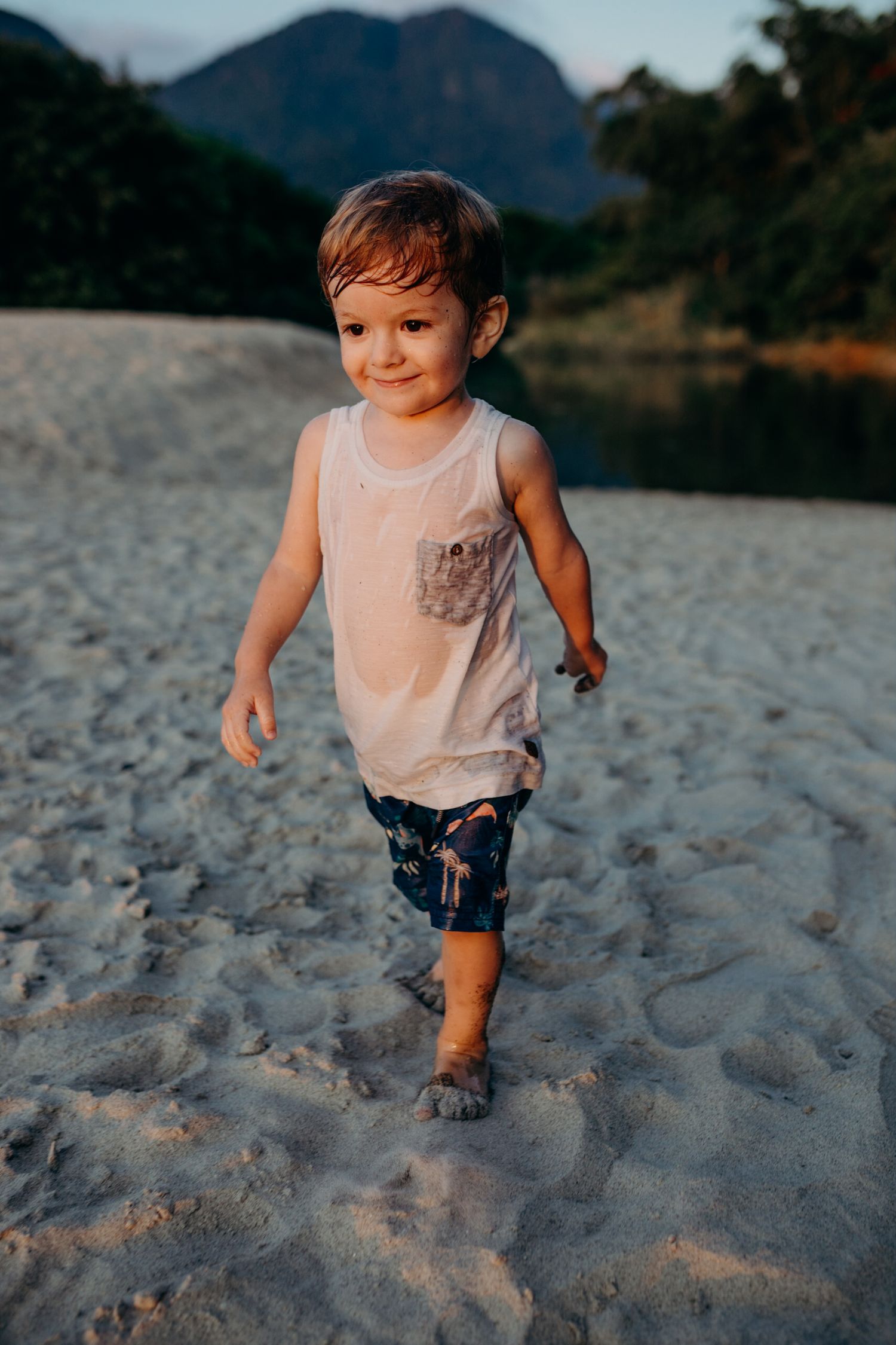 Child running and playing on sandy beach with mountains in background during golden hour.