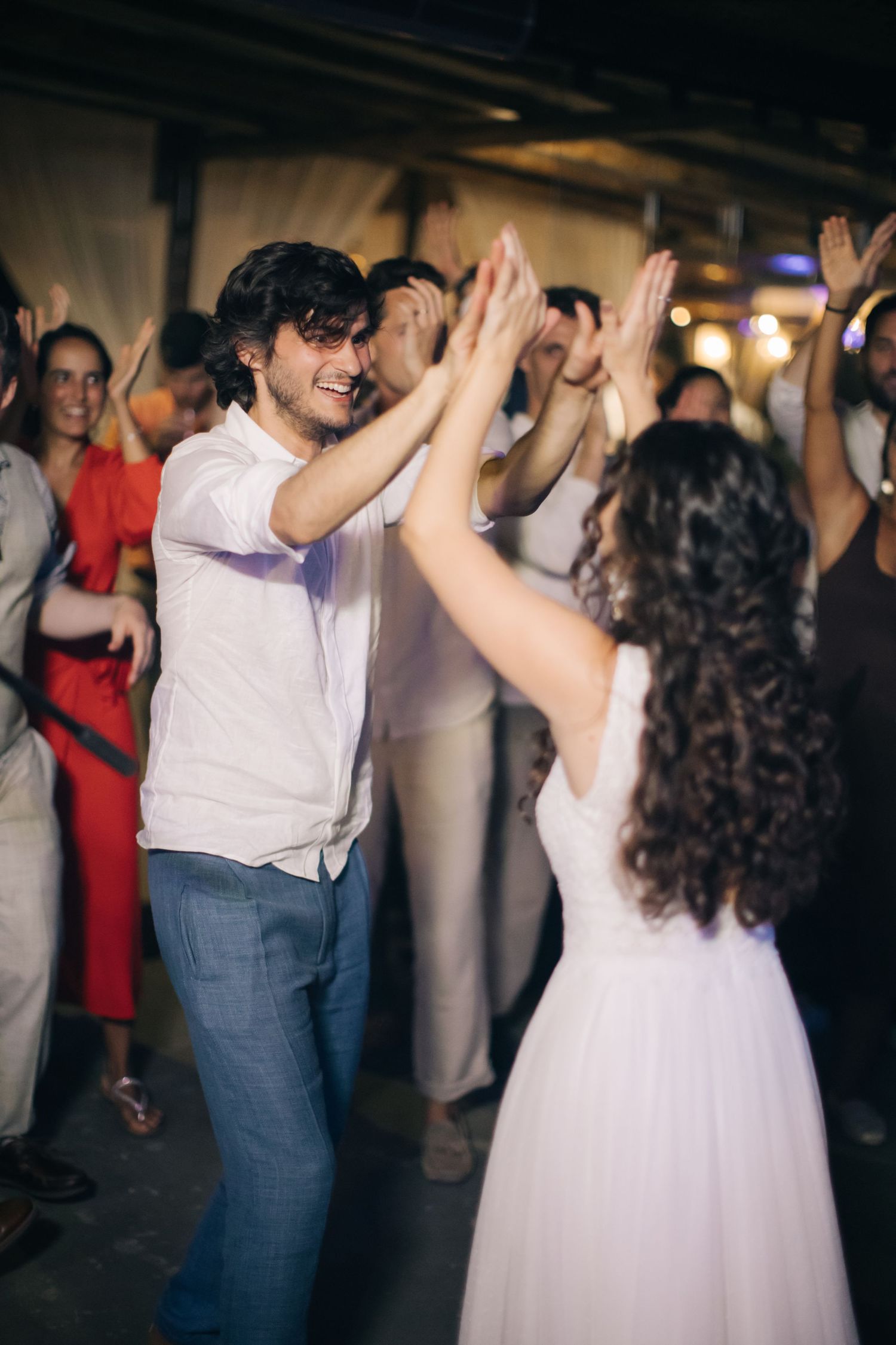 Wedding guests high-fiving and celebrating on the dance floor during an energetic reception moment.