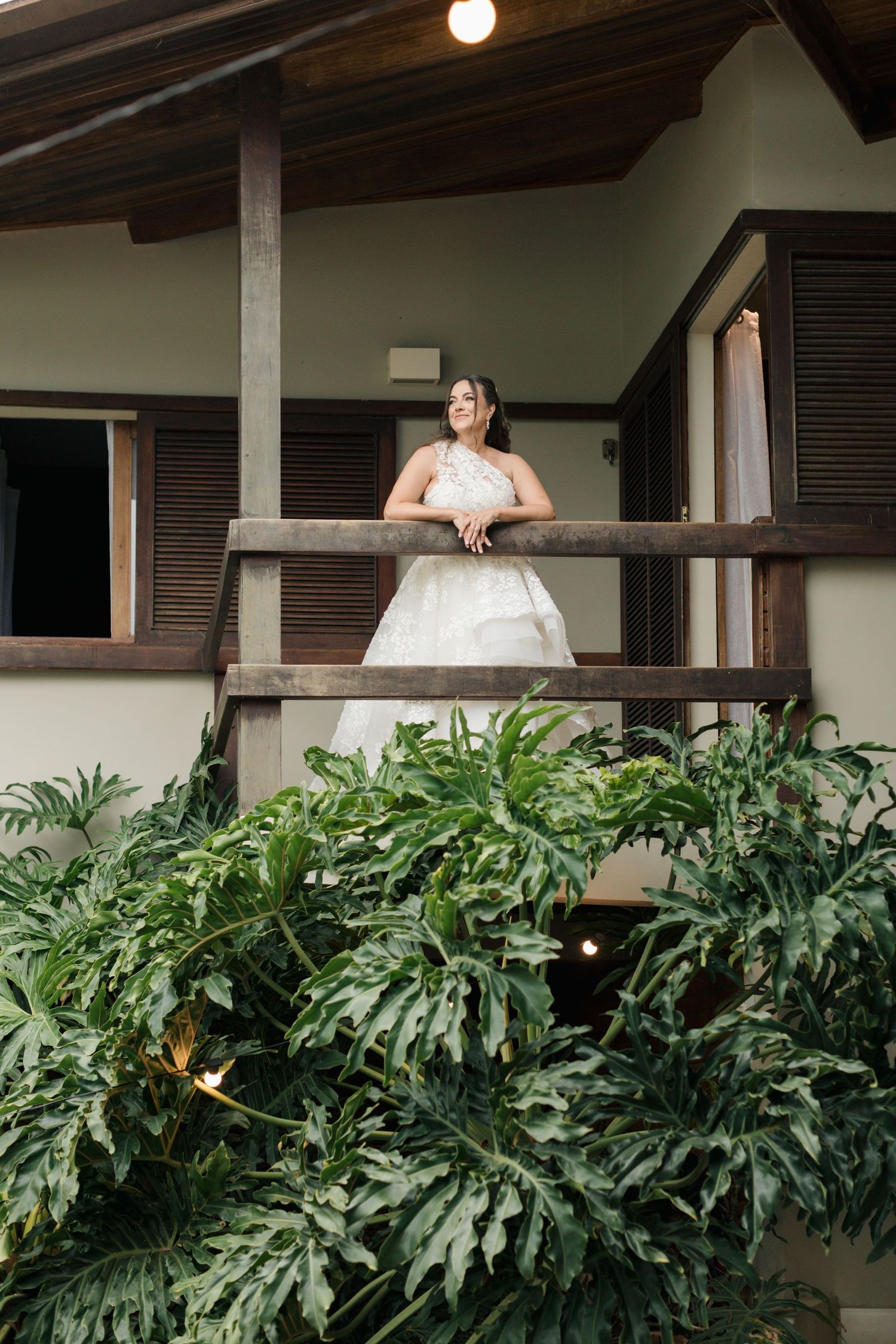 White wooden balcony with lush tropical monstera plants growing beneath on a sunny day.