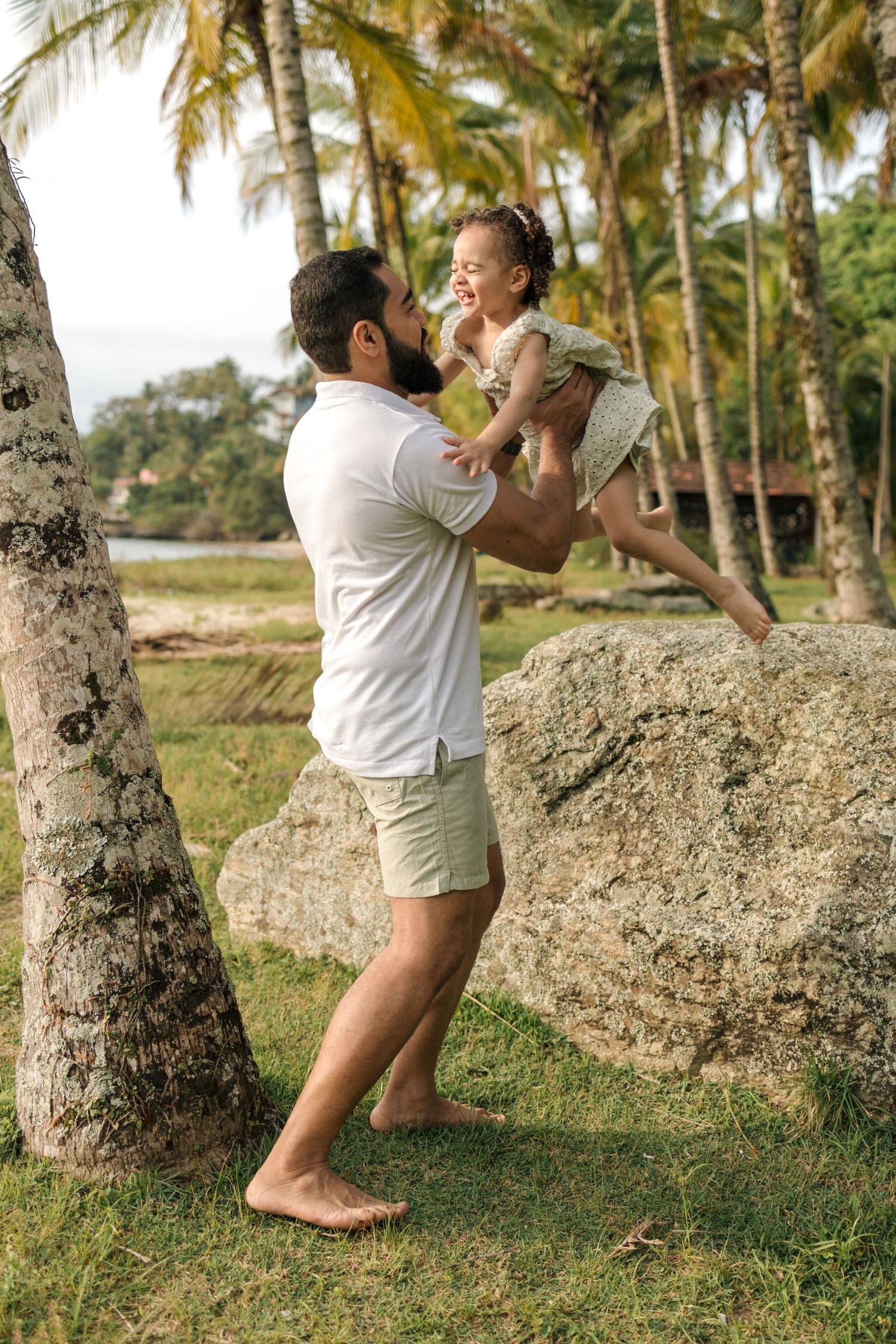 Person climbing and playing around palm tree trunks in a grassy tropical landscape.