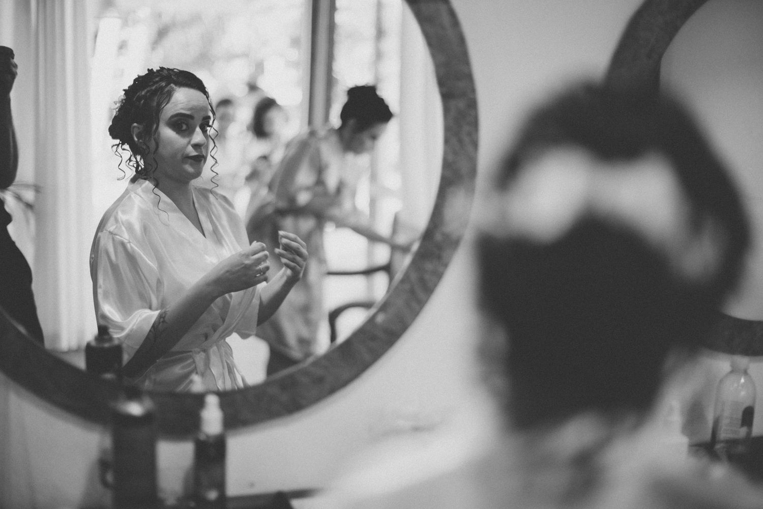 Black and white reflection in a circular mirror showing wedding day preparations.