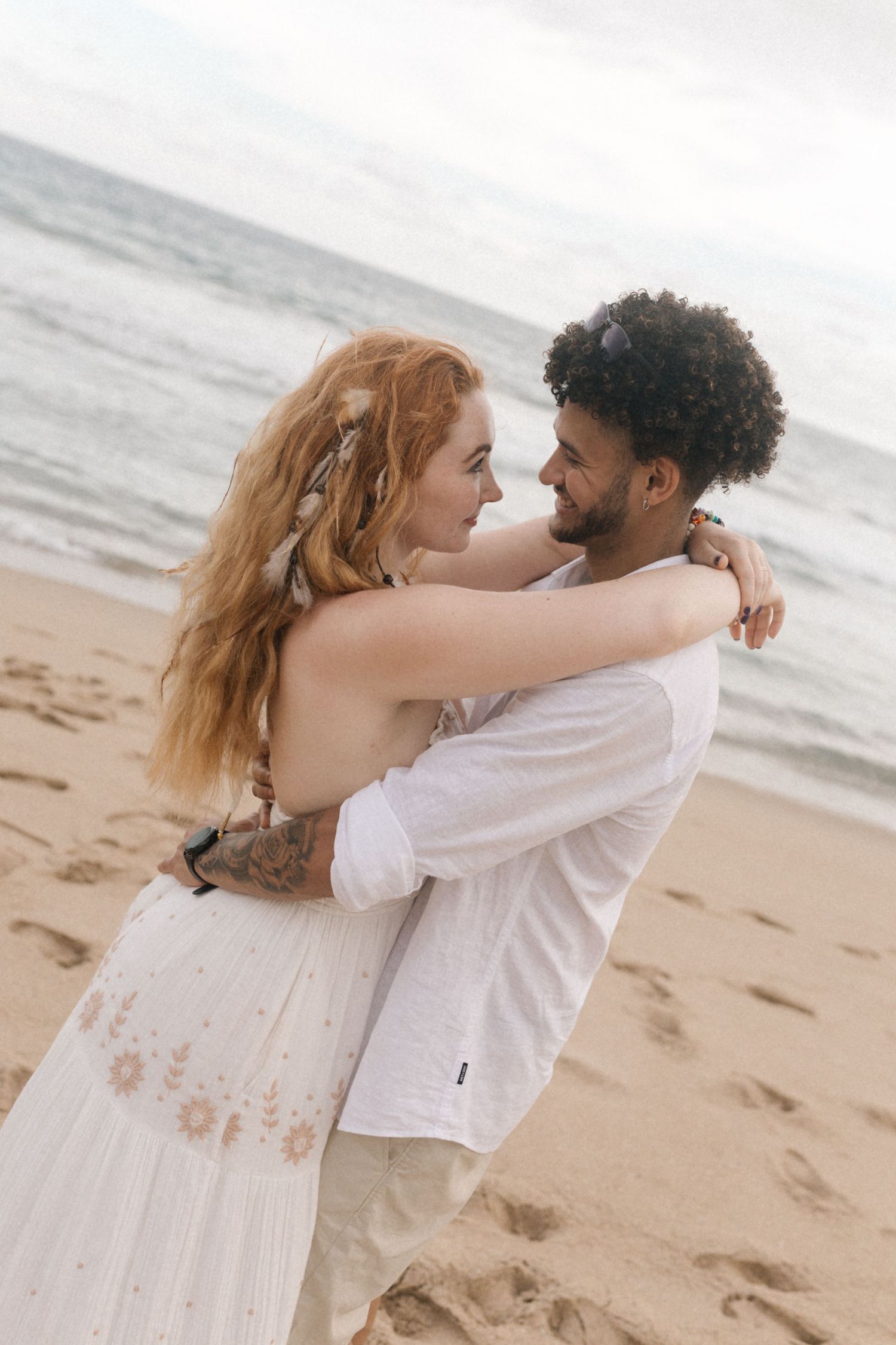 An intimate embrace between newlyweds on a sandy beach with ocean waves in the background.