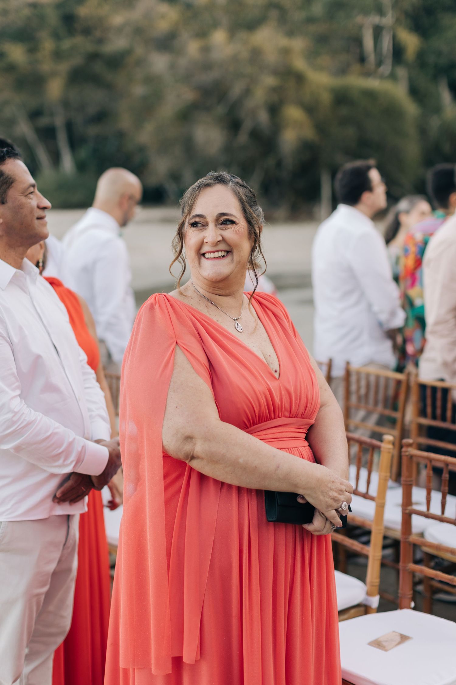 Bridesmaids wearing vibrant coral-colored dresses stand at an outdoor wedding venue.