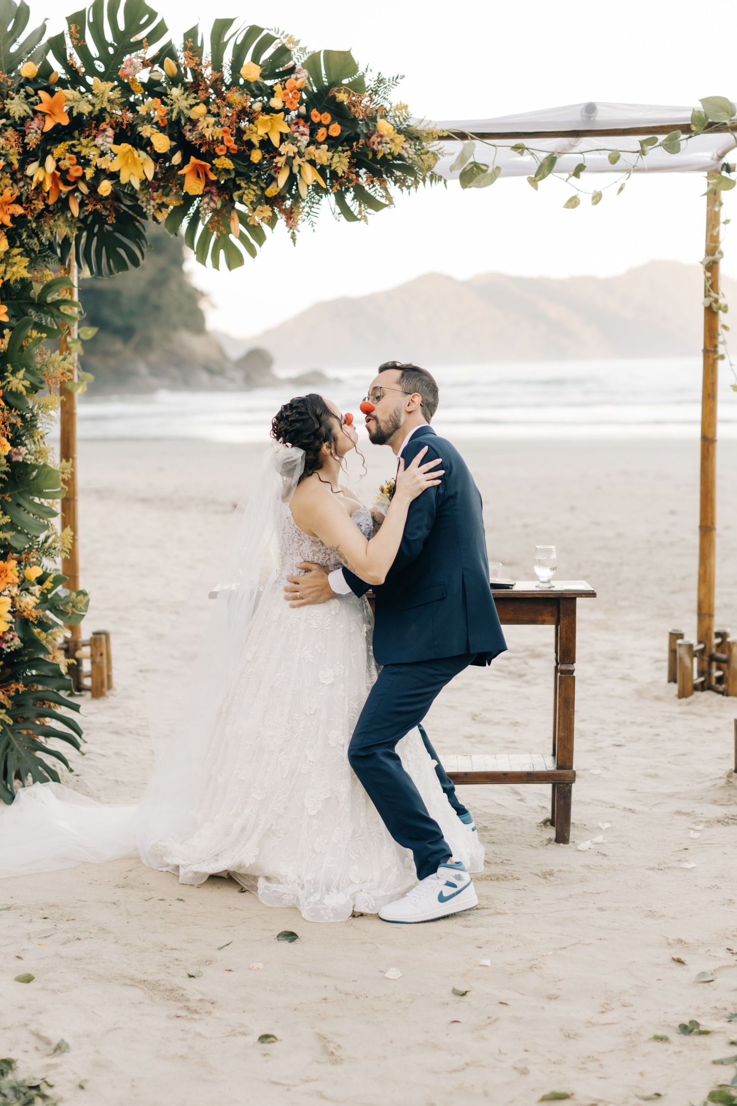 Wedding couple shares a romantic dance moment under a floral arch on a misty beach.