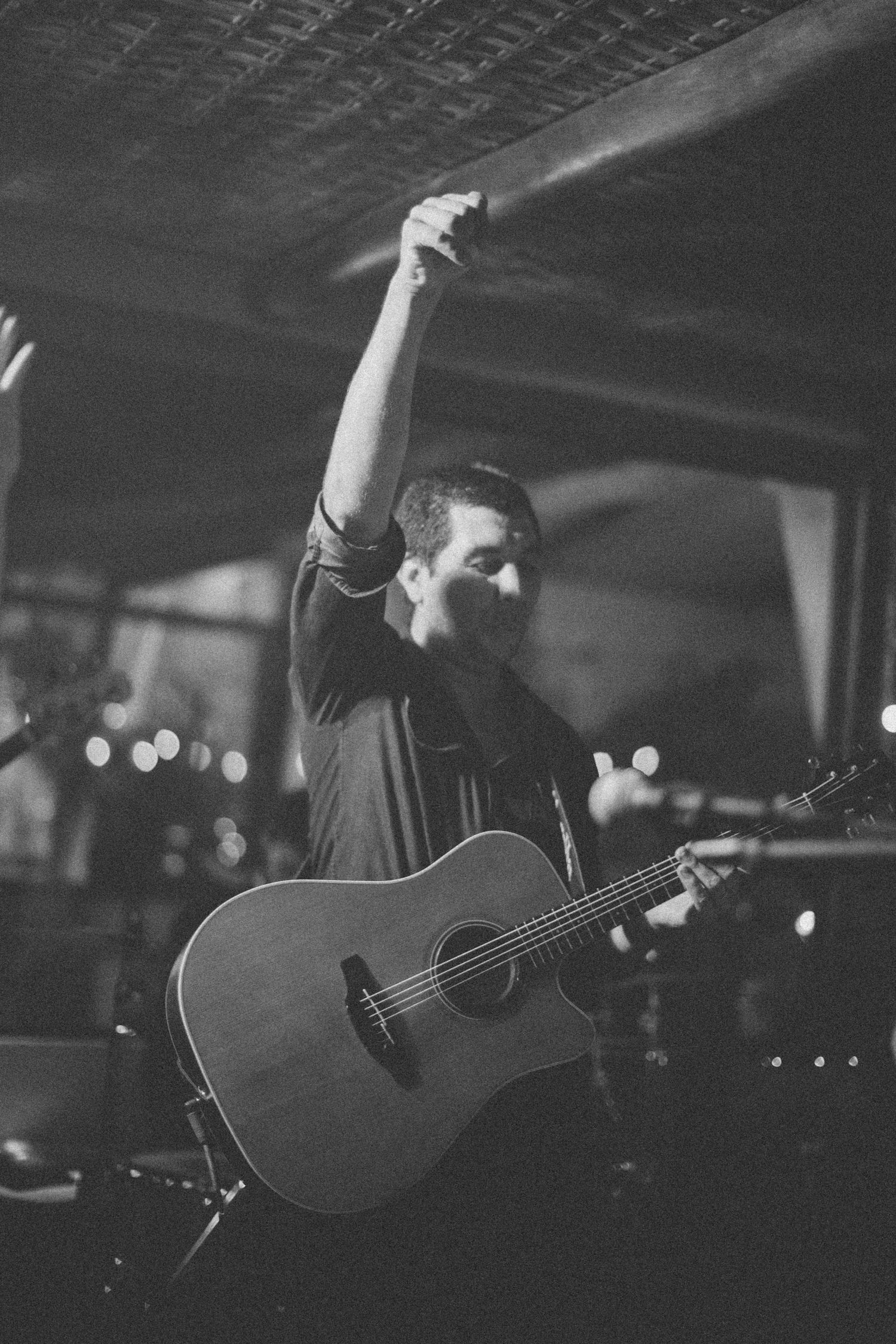 Musician in black shirt performs passionately on acoustic guitar at dimly lit venue.
