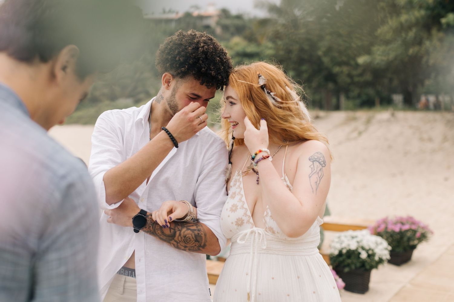 An emotional wedding moment shared between a couple on a beach with pink flowers.