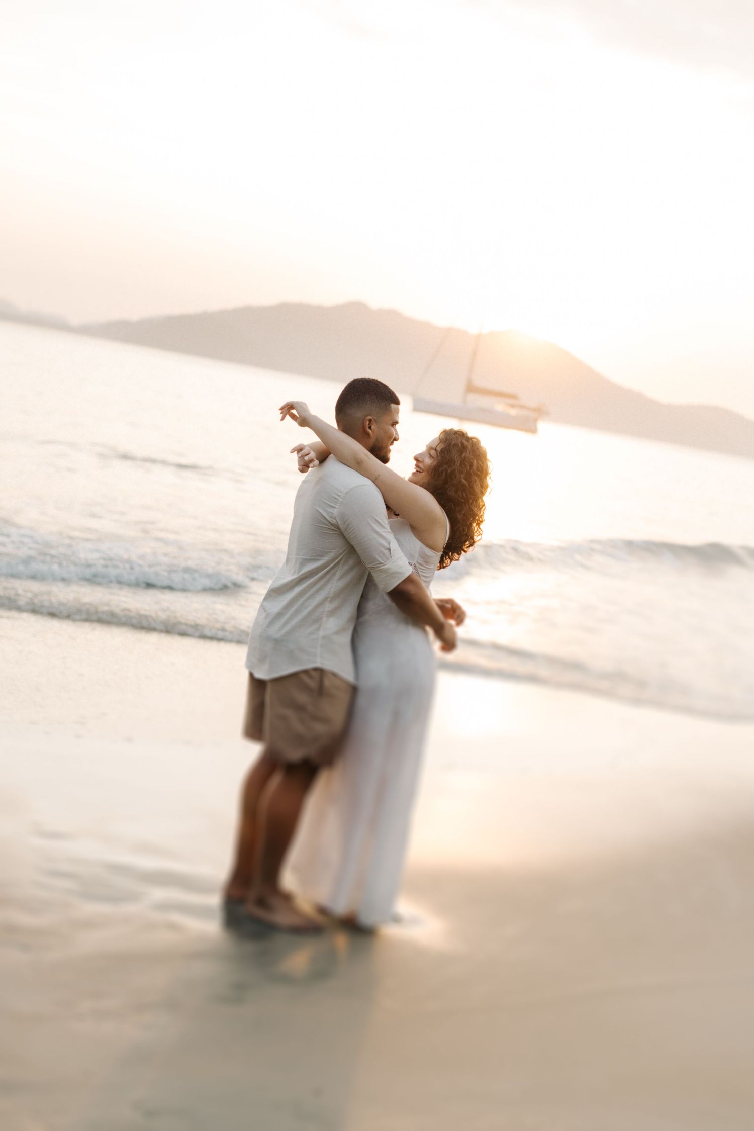 Couple in light colored clothing dancing in shallow water at sunset beach.