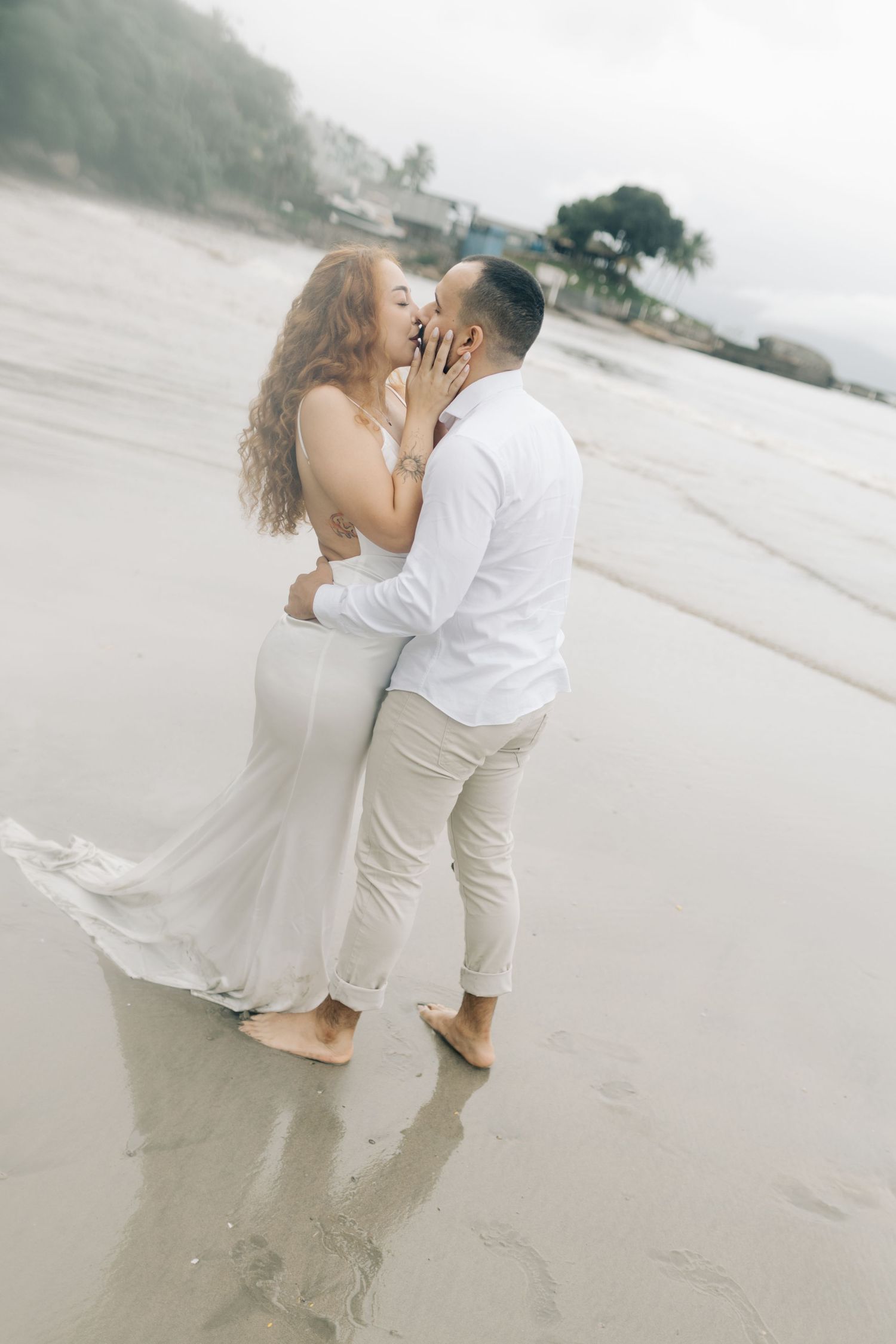 A couple shares a passionate moment on a misty beach, their reflection visible in the wet sand.