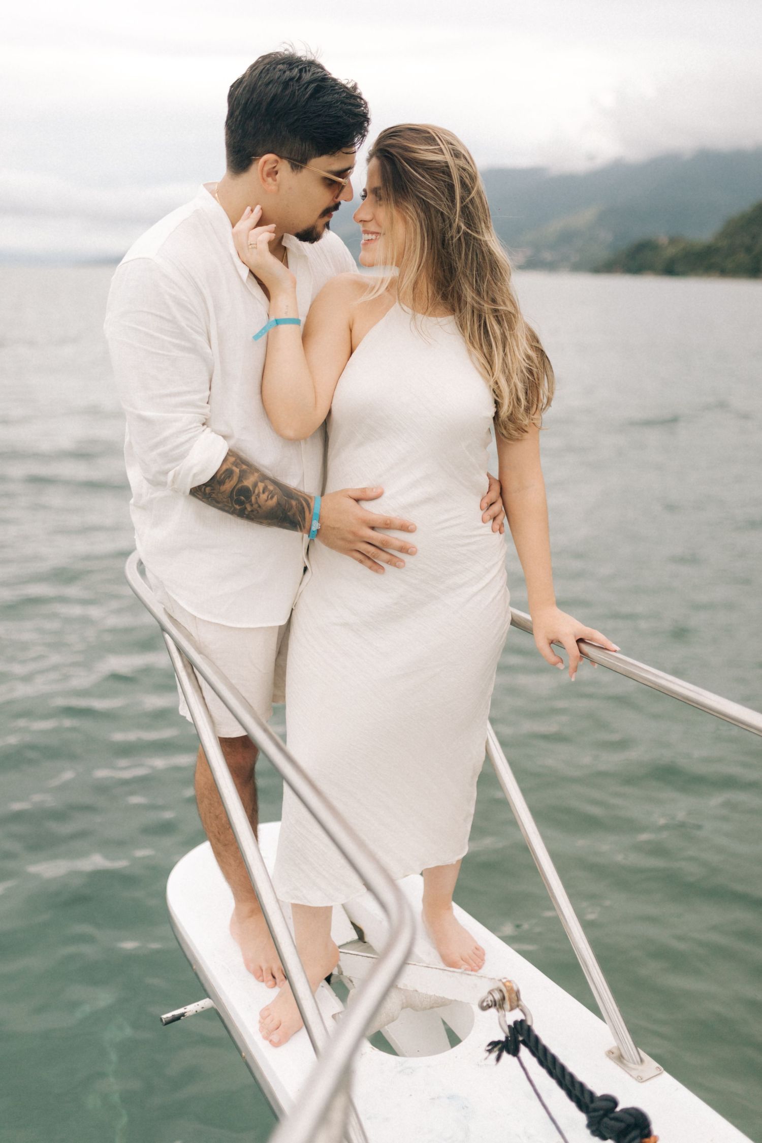 Romantic couple sharing tender moment on boat deck with mountain lake scenery.