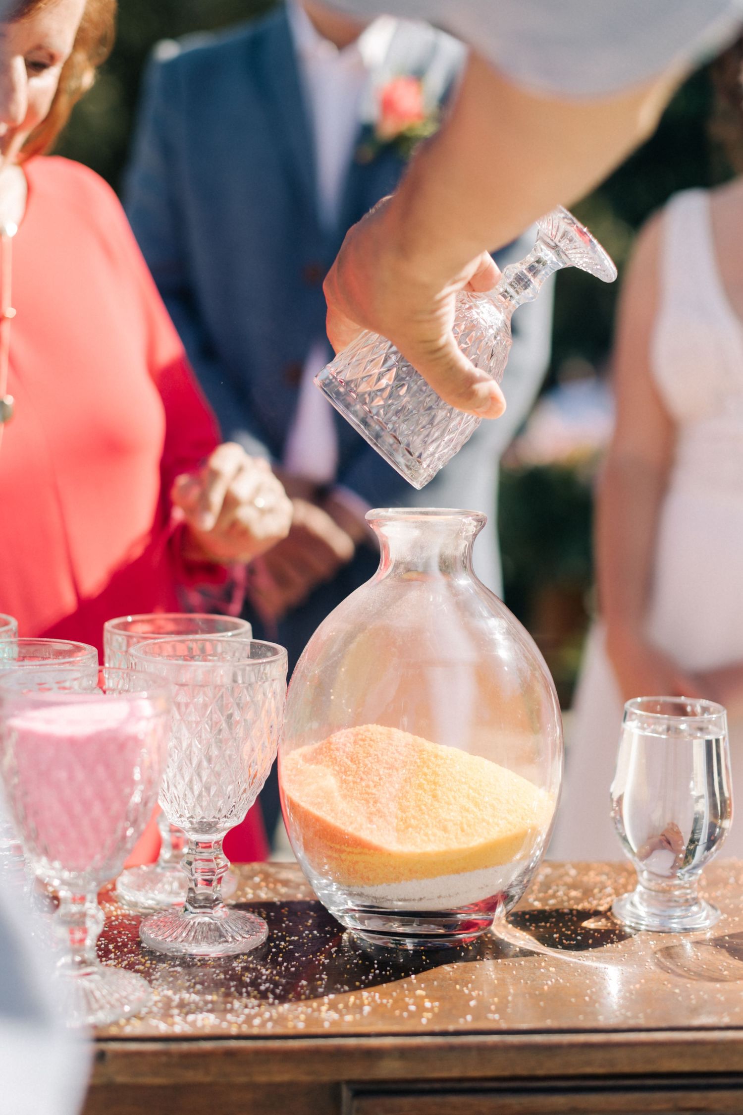 Hands pour colorful drinks into vintage crystal glassware at wedding reception.