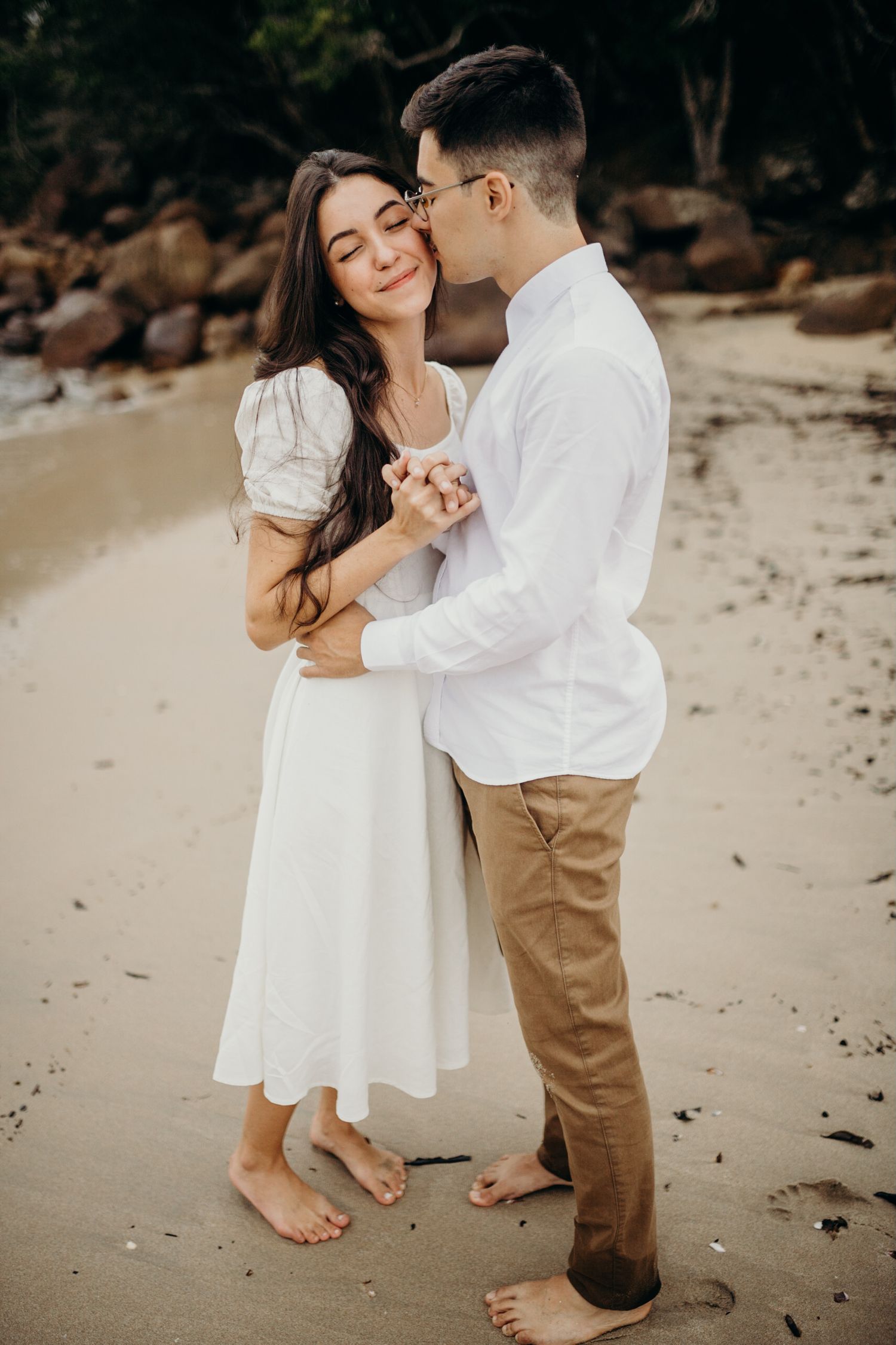 A couple shares intimate moments on a beach during their engagement photography session.