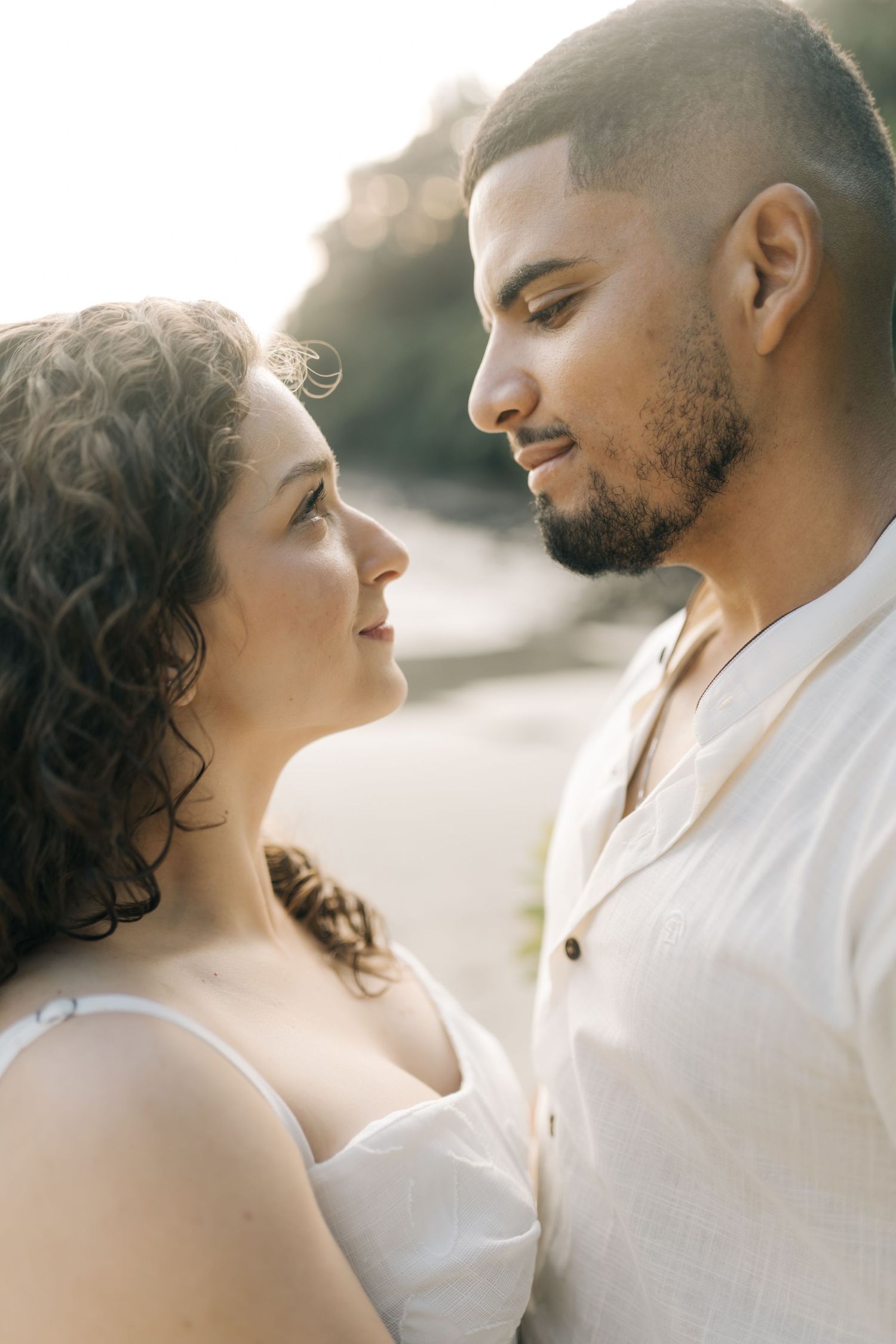 A romantic couple in white outfits gazing at each other during a sunset photoshoot.
