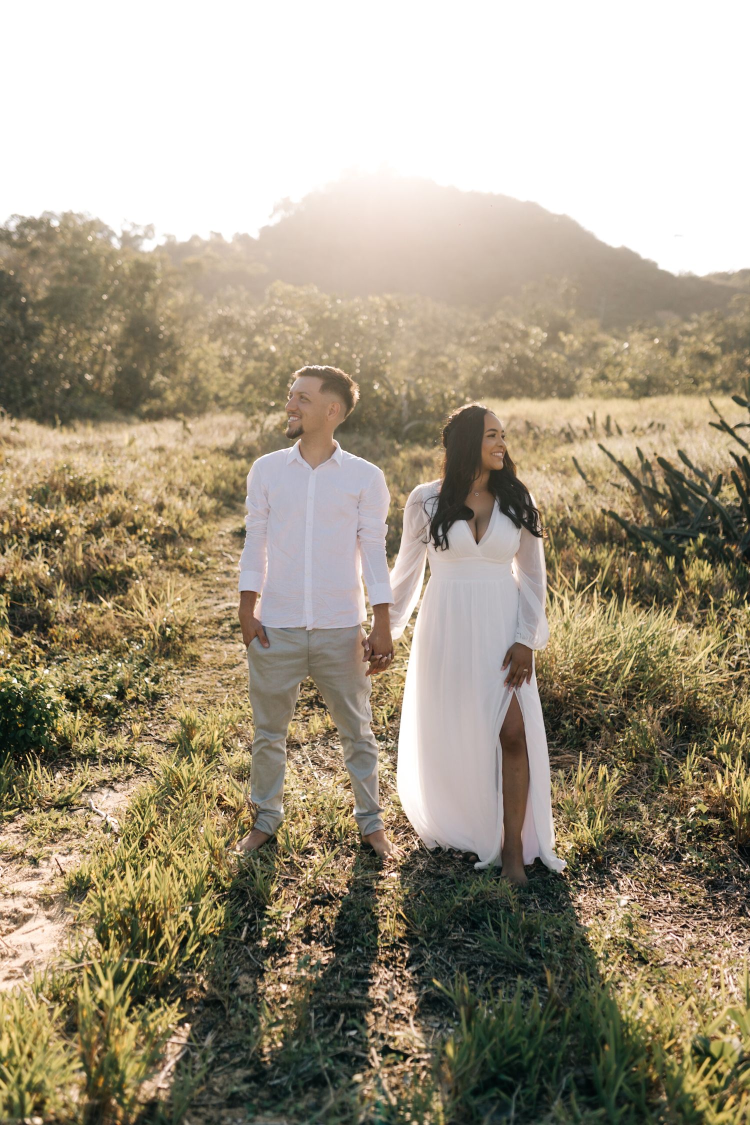 A couple in white attire walks together on a scenic trail during golden hour.