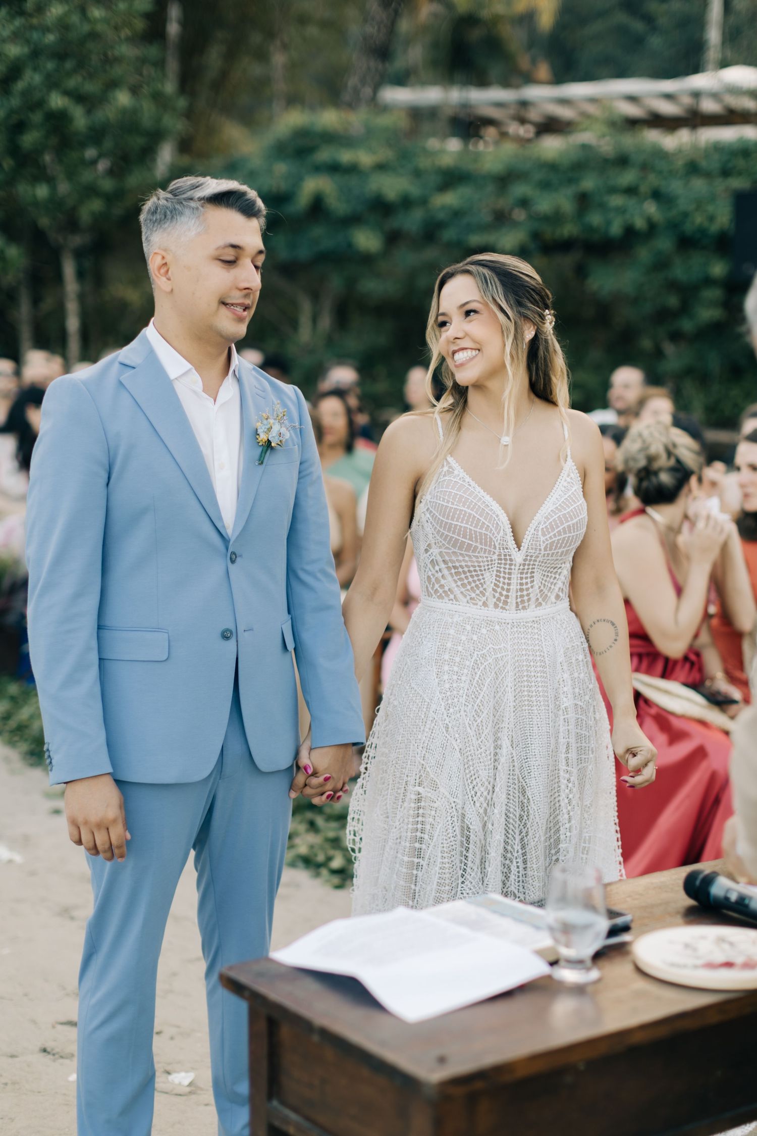 A couple stands at a wooden ceremony table during their outdoor beach wedding.