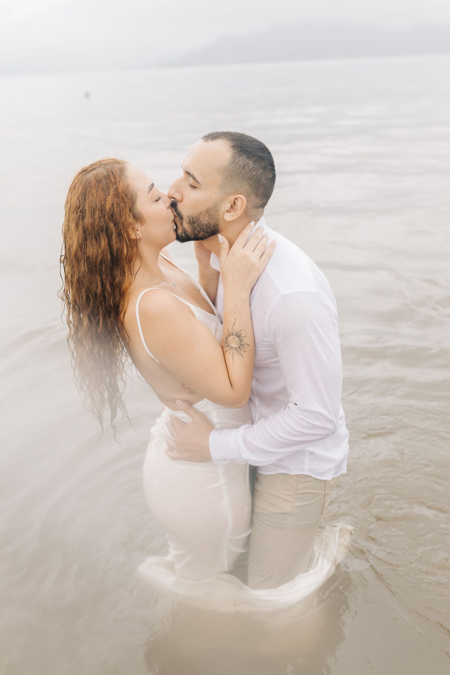 A couple shares an intimate kiss while standing in shallow ocean water.