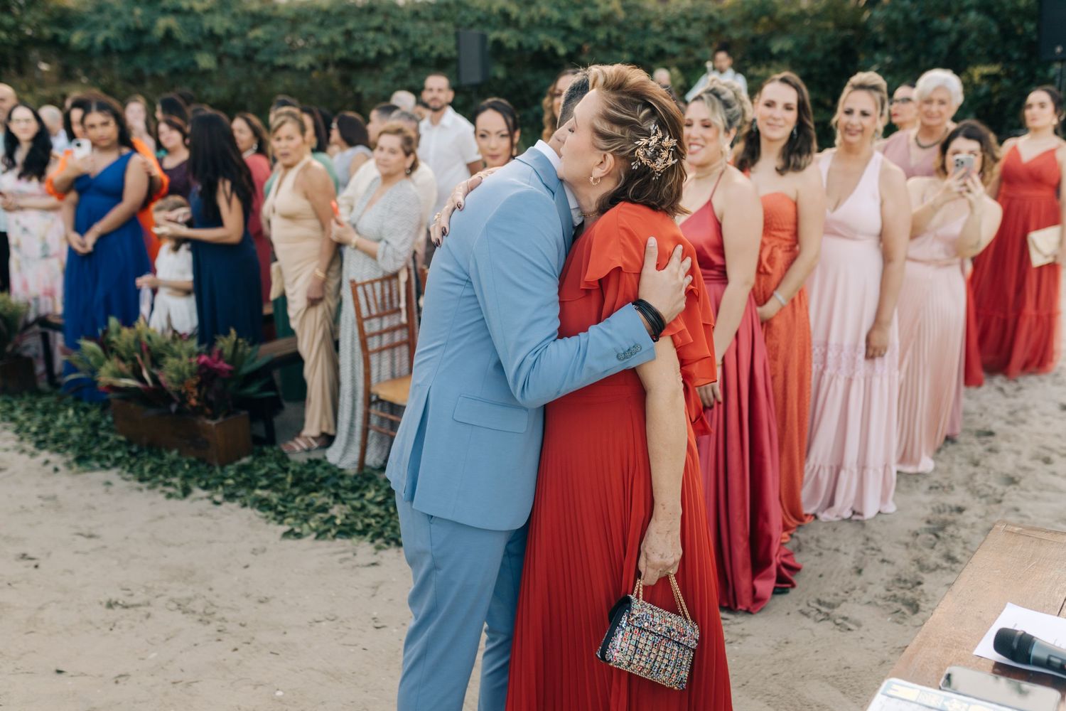 Wedding guests in formal attire watching an emotional moment during outdoor ceremony.