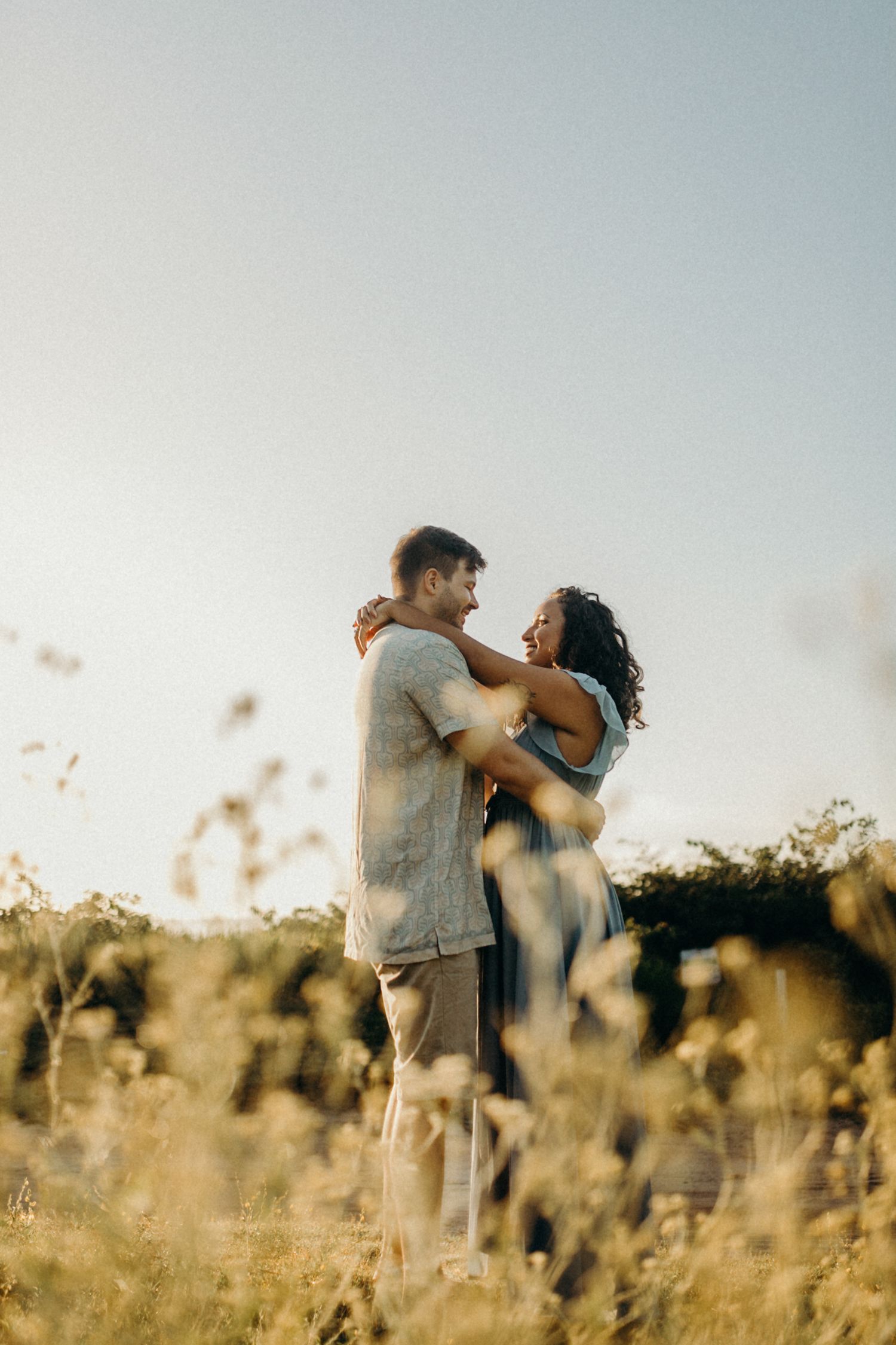 Silhouetted couple embracing in golden field during sunset.