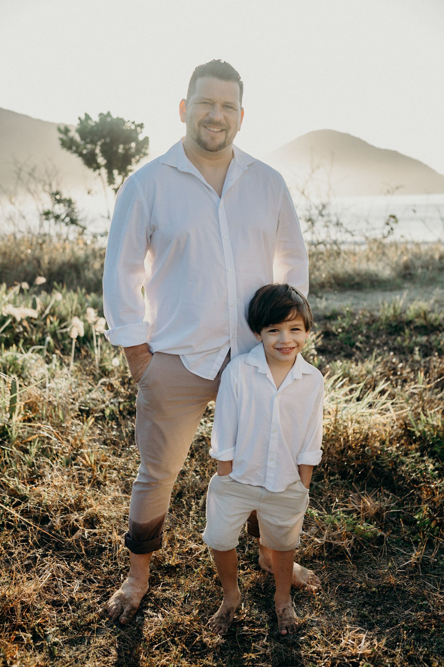 A parent and child pose together on a hillside with mountains in the background.