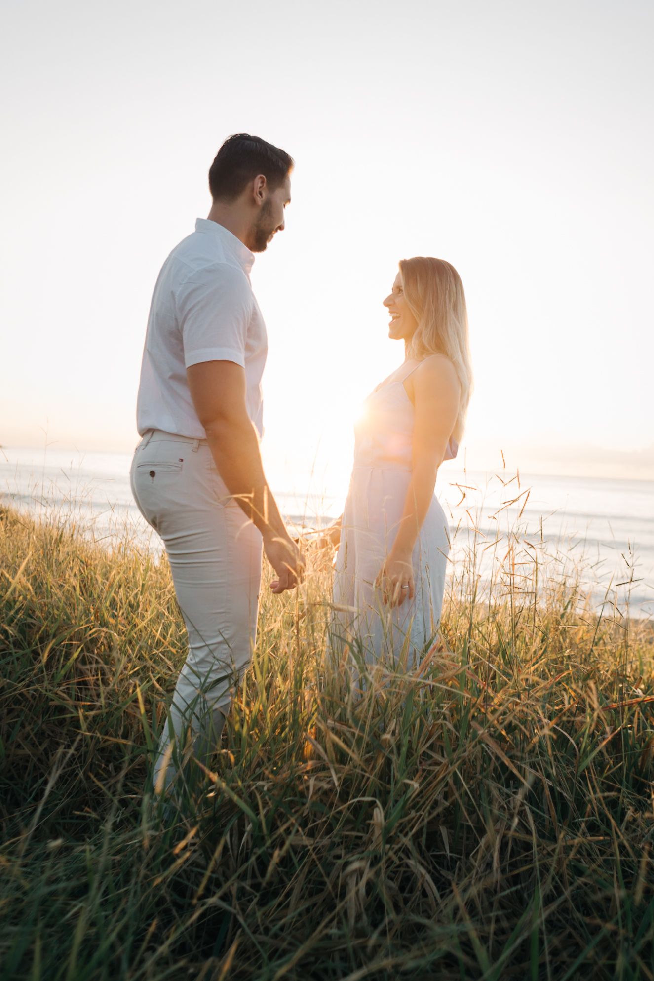 Romantic couple sharing tender moments in a grassy field by the beach at sunset.