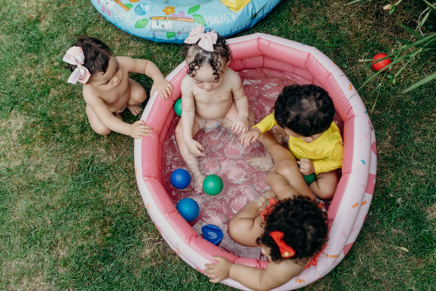 Multiple kids splashing and playing together in a small backyard kiddie pool.