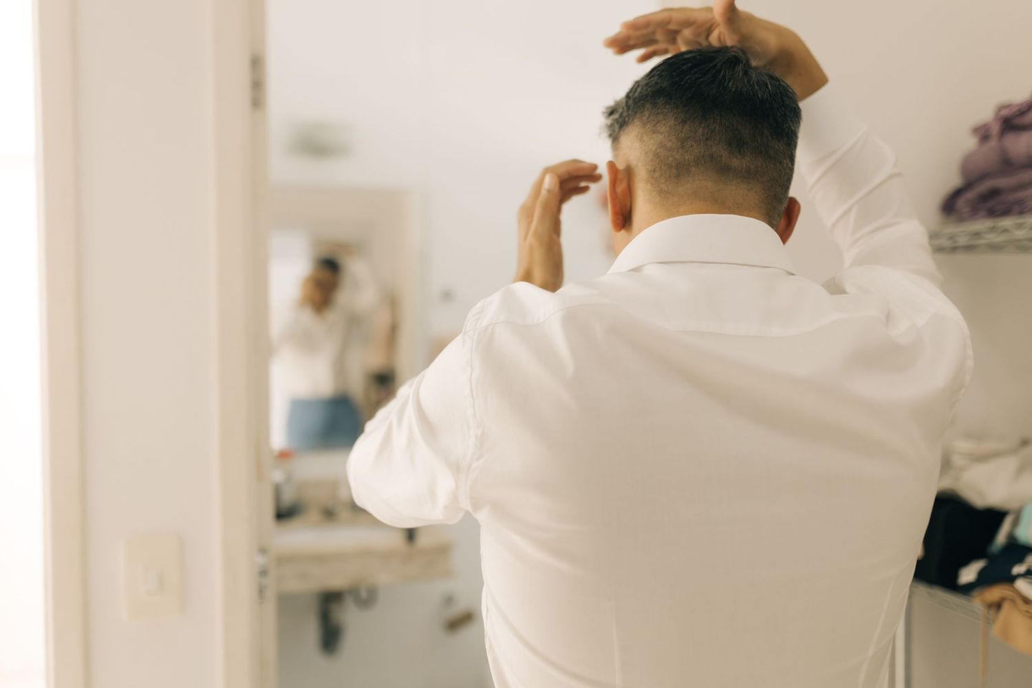 Back view of person in white shirt fixing hair in mirror.