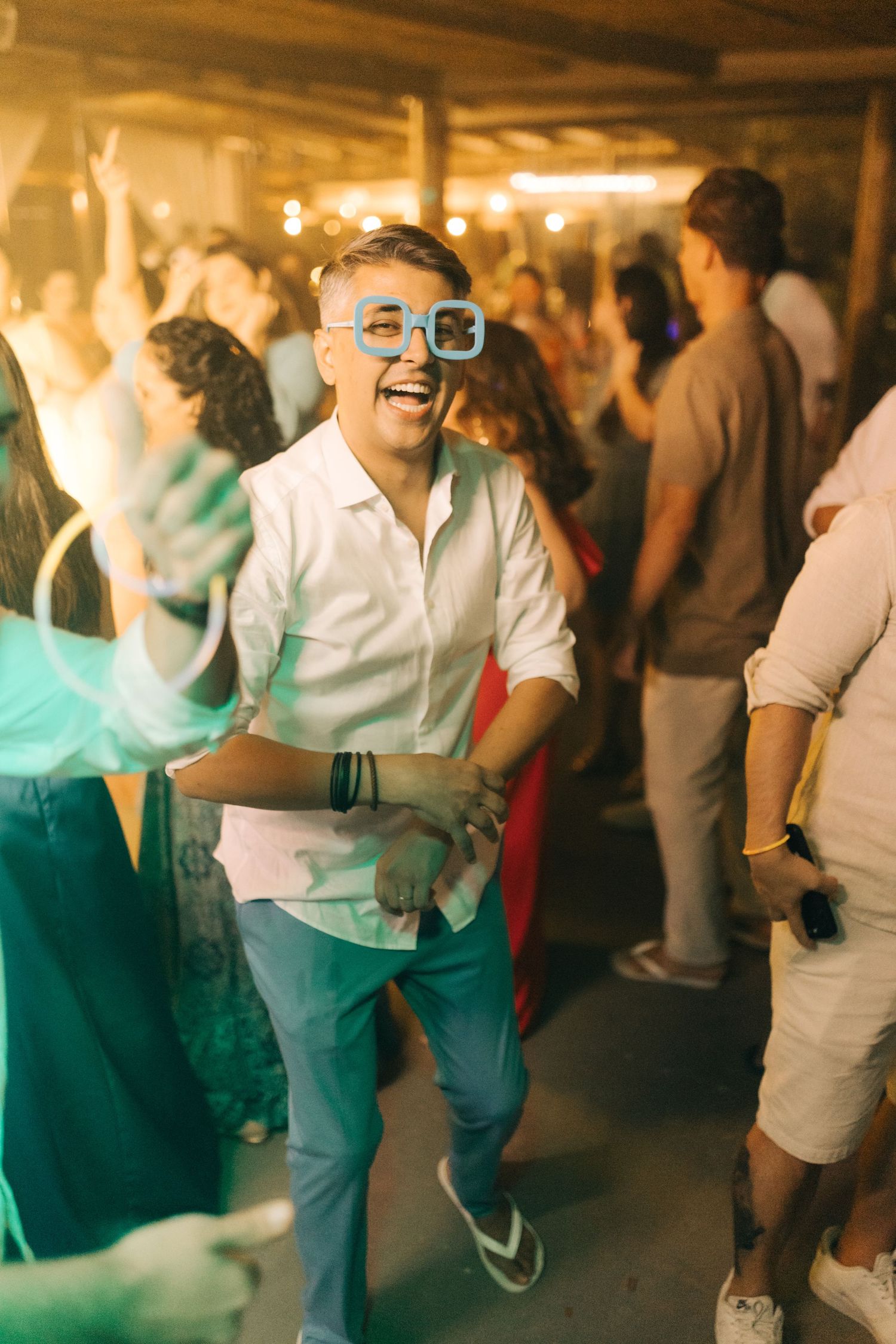 Guest wearing blue sunglasses dances at lively indoor party.
