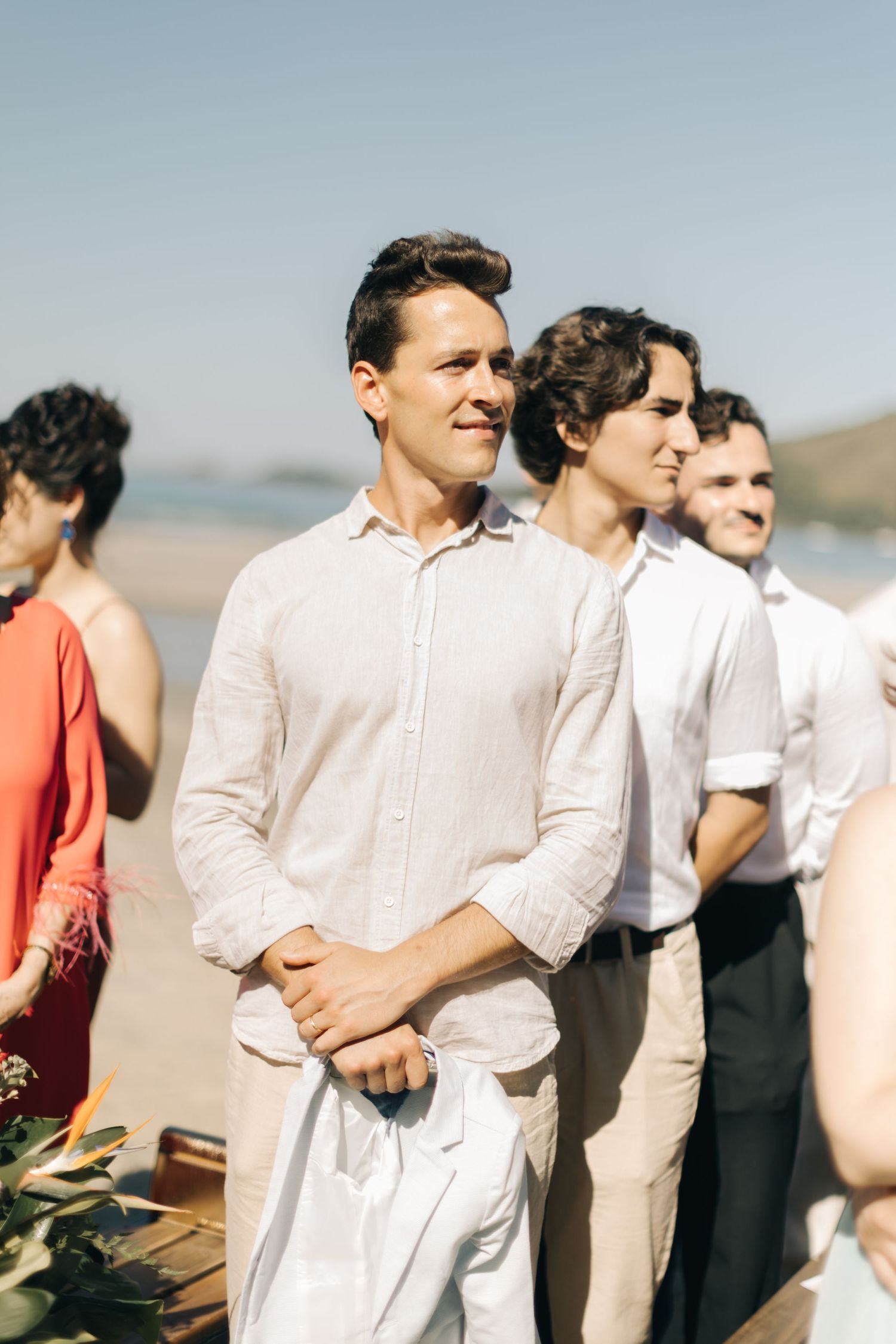 Wedding party members in crisp white shirts and light colored attire stand in formation outdoors.