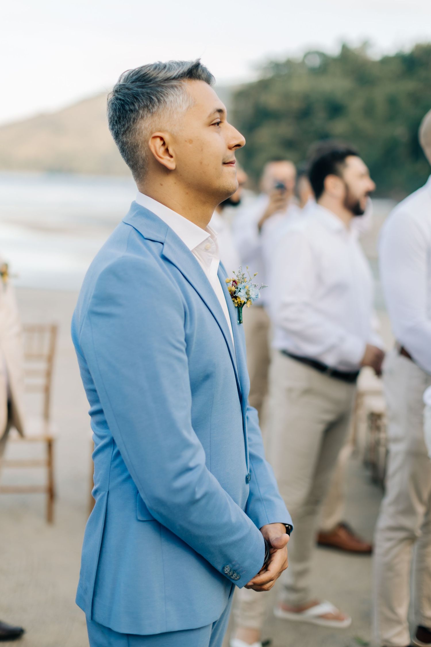 Person in light blue suit standing on beach during wedding ceremony.