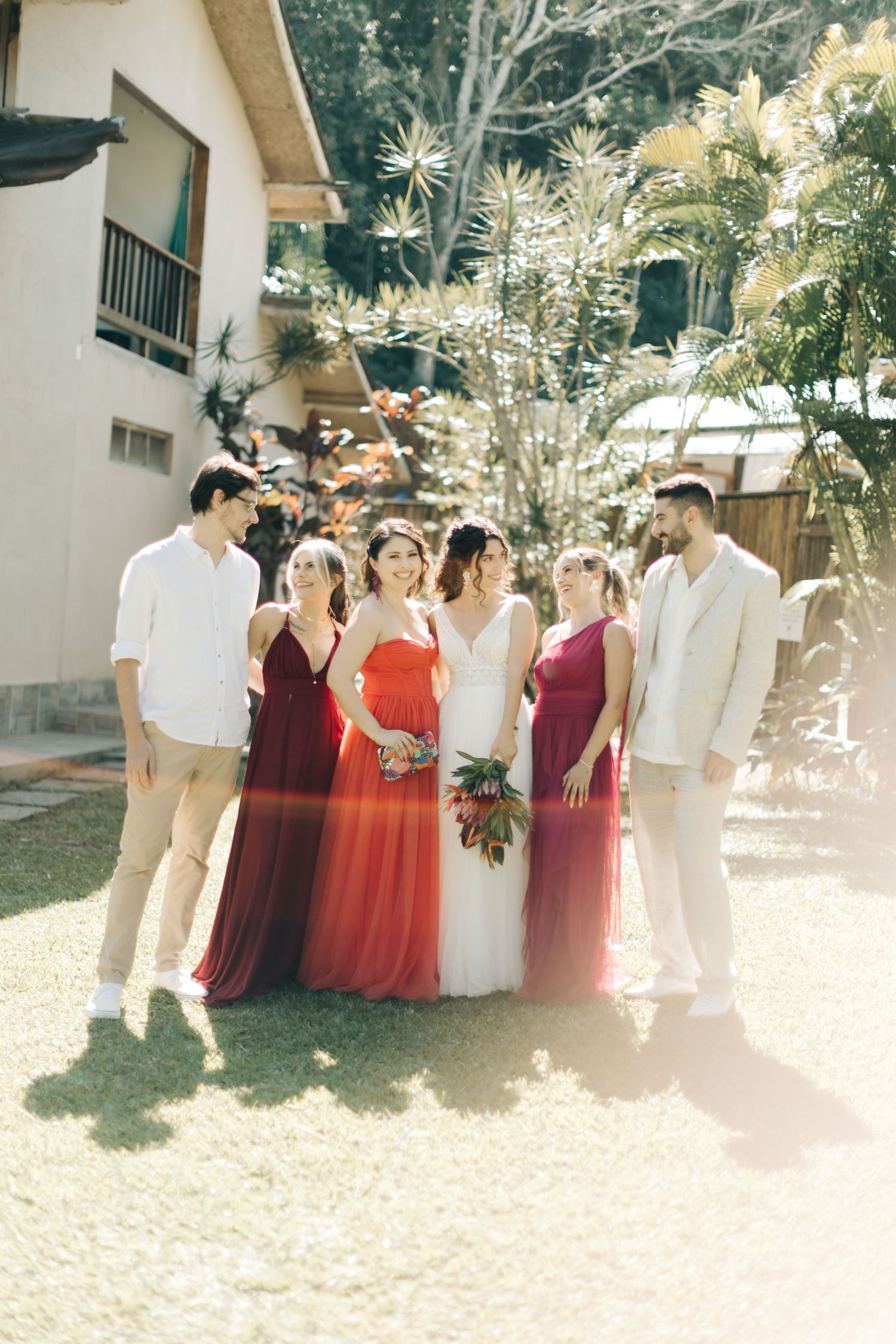 Wedding party in coordinating white, burgundy and coral attire posing together in a garden setting.