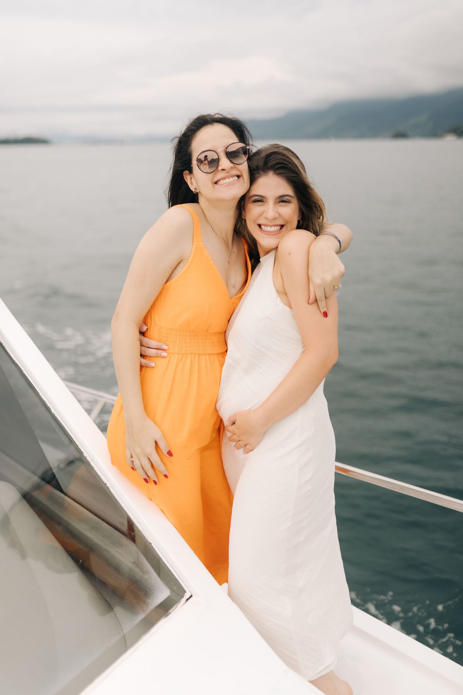 Two people sharing a joyful embrace while standing on a boat deck with mountains in the background.