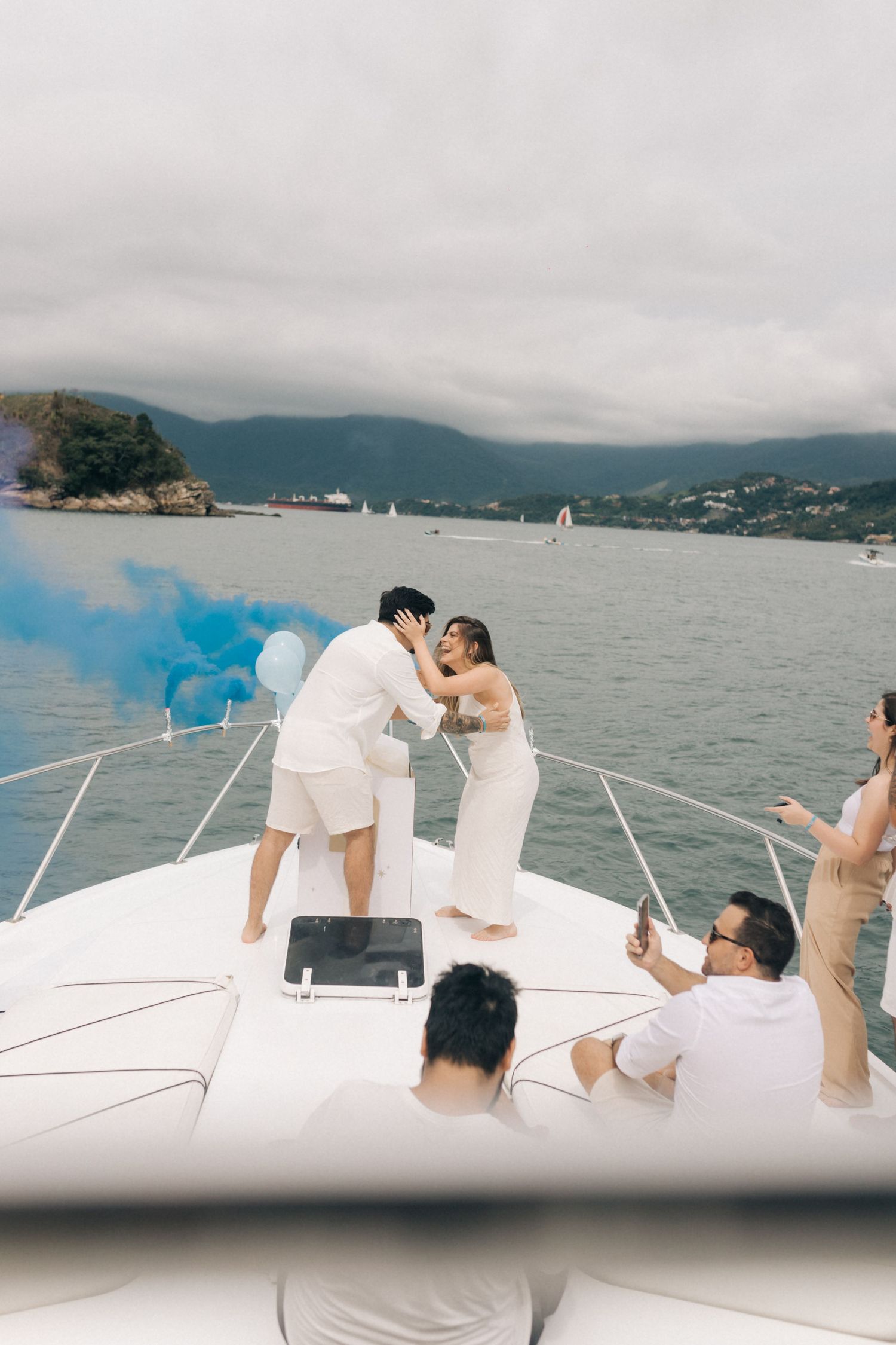 Tender moment shared during boat celebration with blue smoke and mountain backdrop.