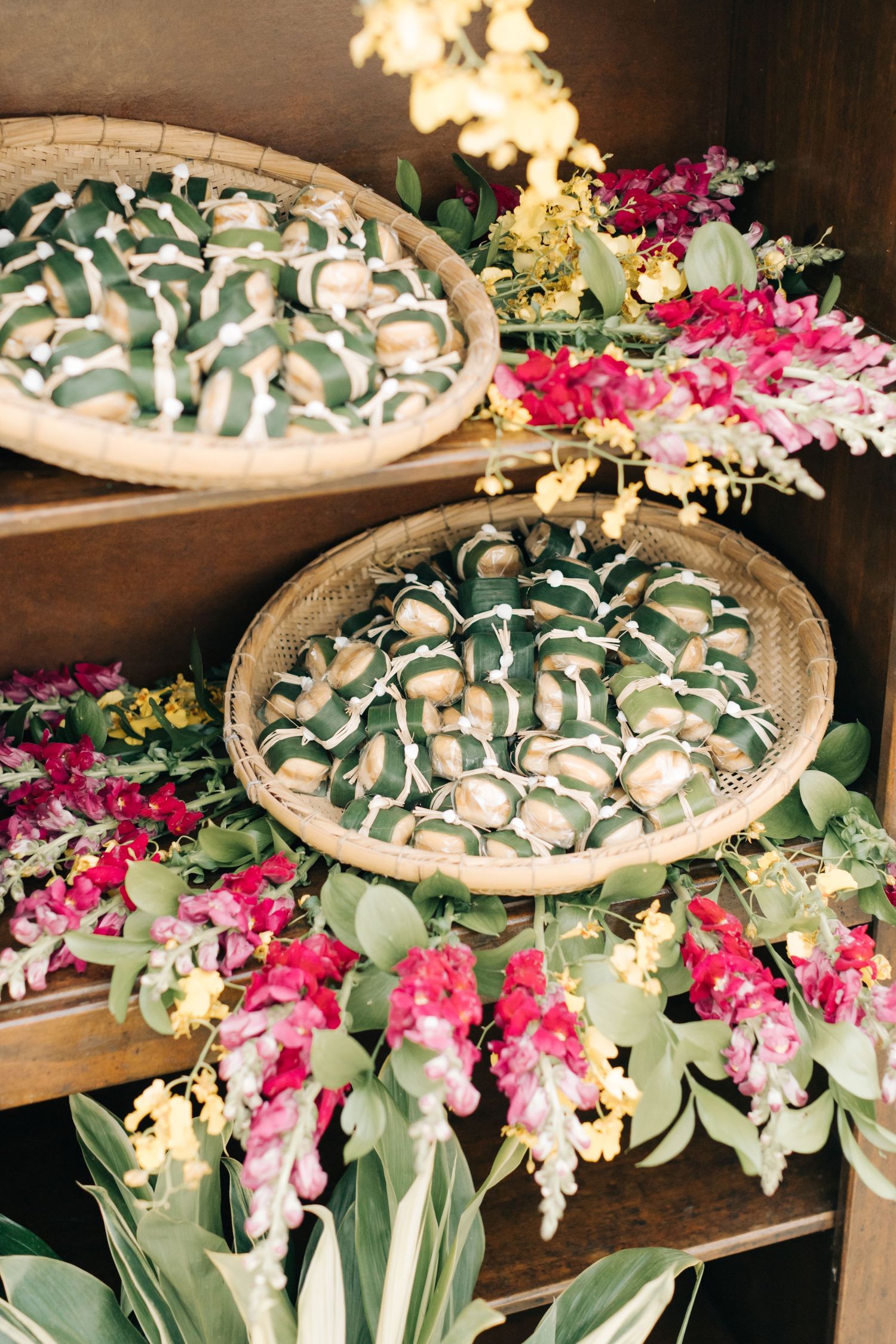 Decorative baskets adorned with tropical leaves and pink orchids arranged on wooden shelves.