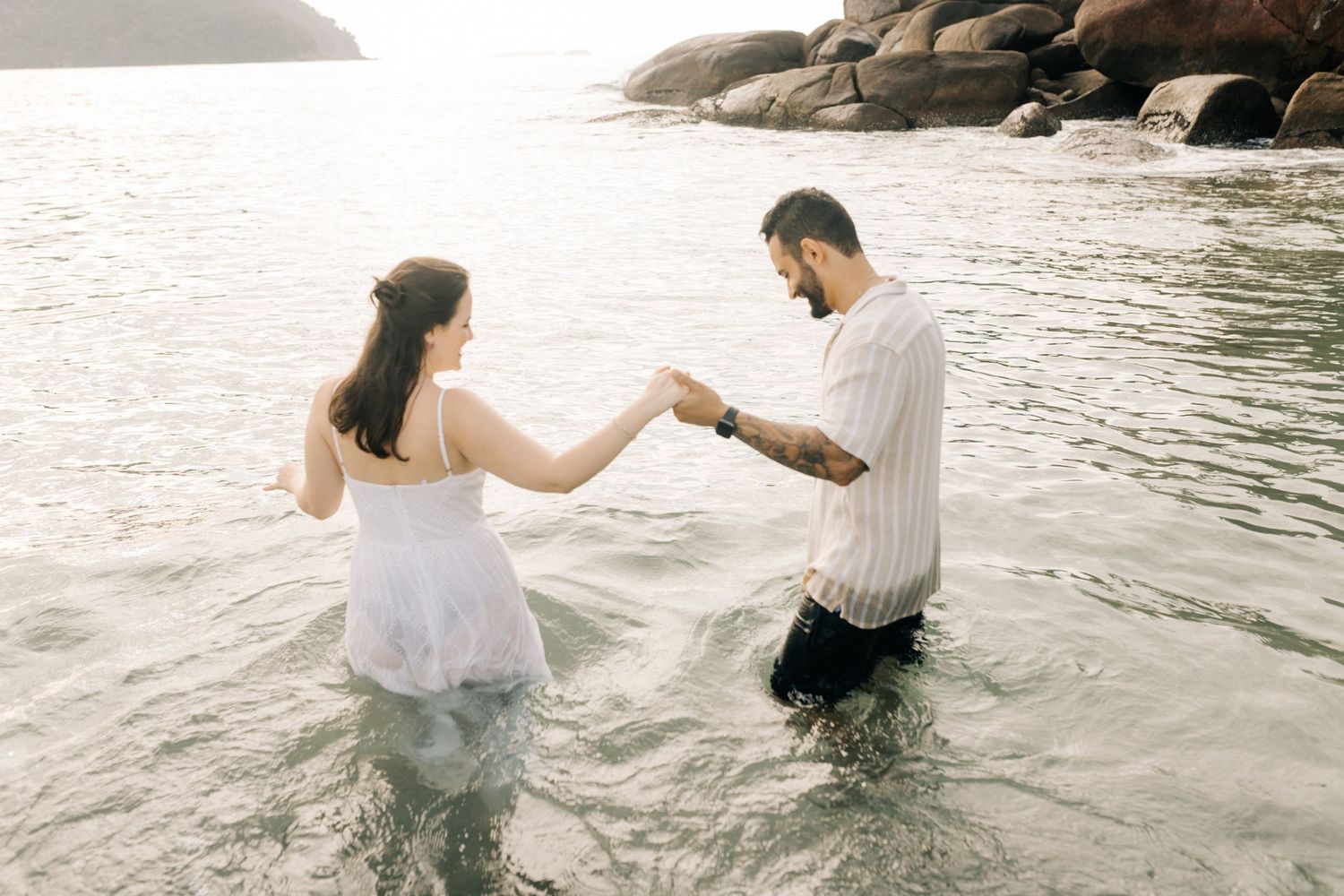 A romantic couple plays and splashes in the shallow ocean water.