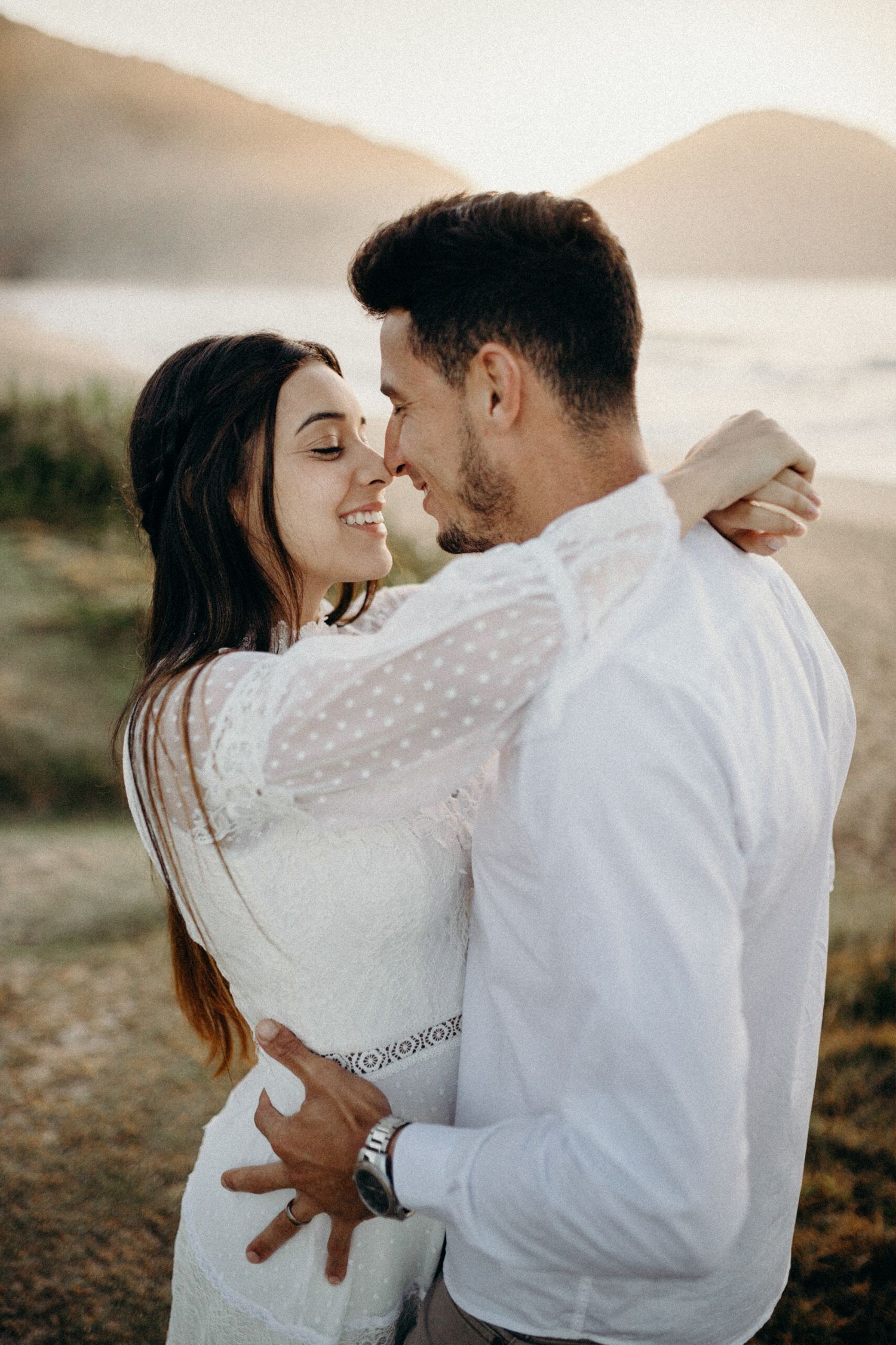 Close embrace between couple wearing white against ocean backdrop.