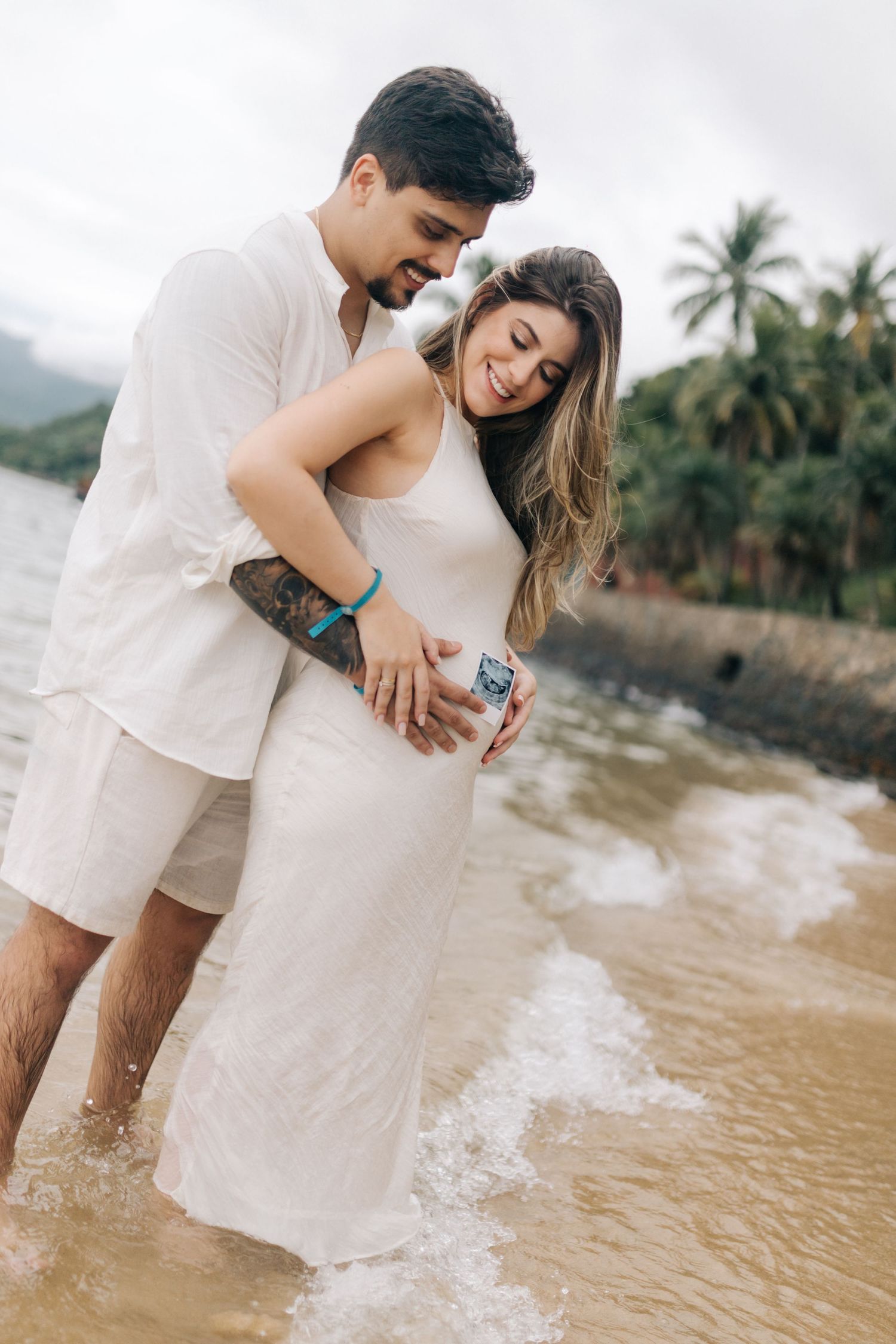 A couple shares a joyful moment on a tropical beach with palm trees in the background.