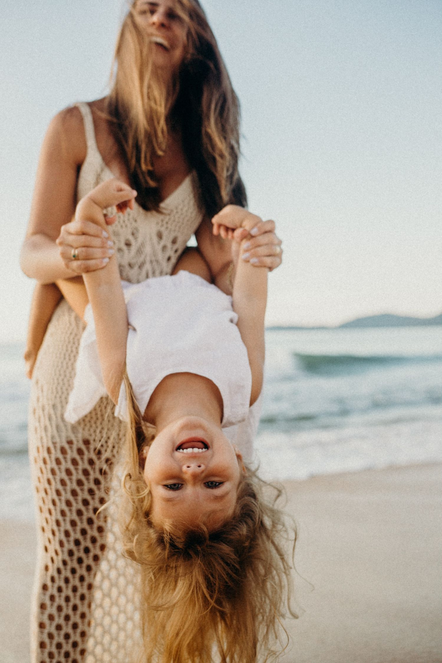 Fun beach photo with laughing child held upside down against sunset ocean backdrop.