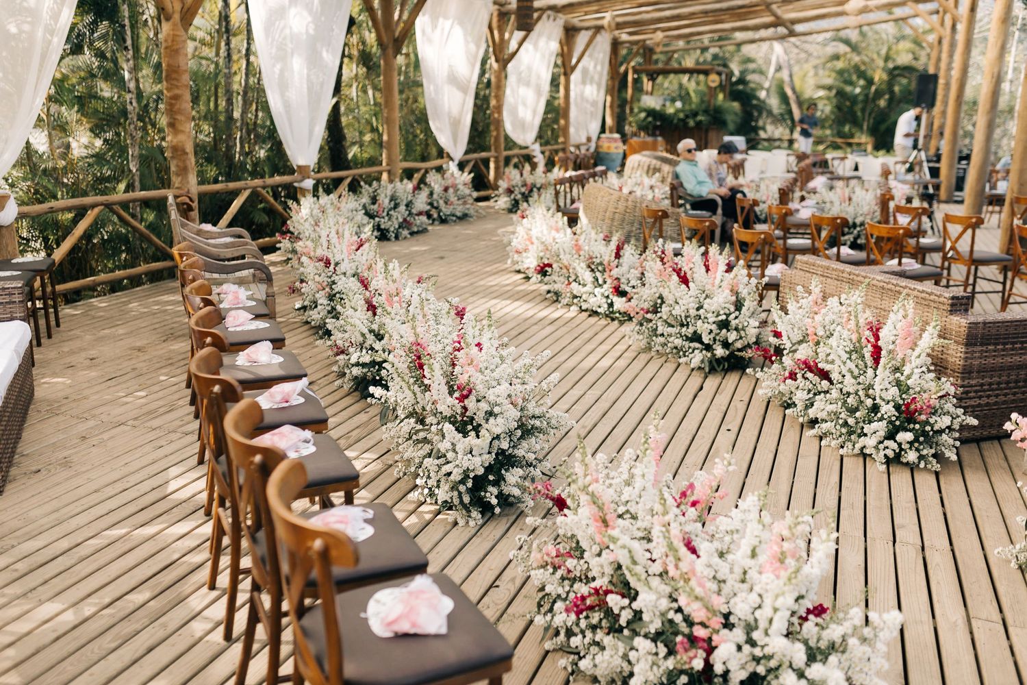 Wedding reception setup with wooden chairs and floral arrangements under a covered outdoor space.