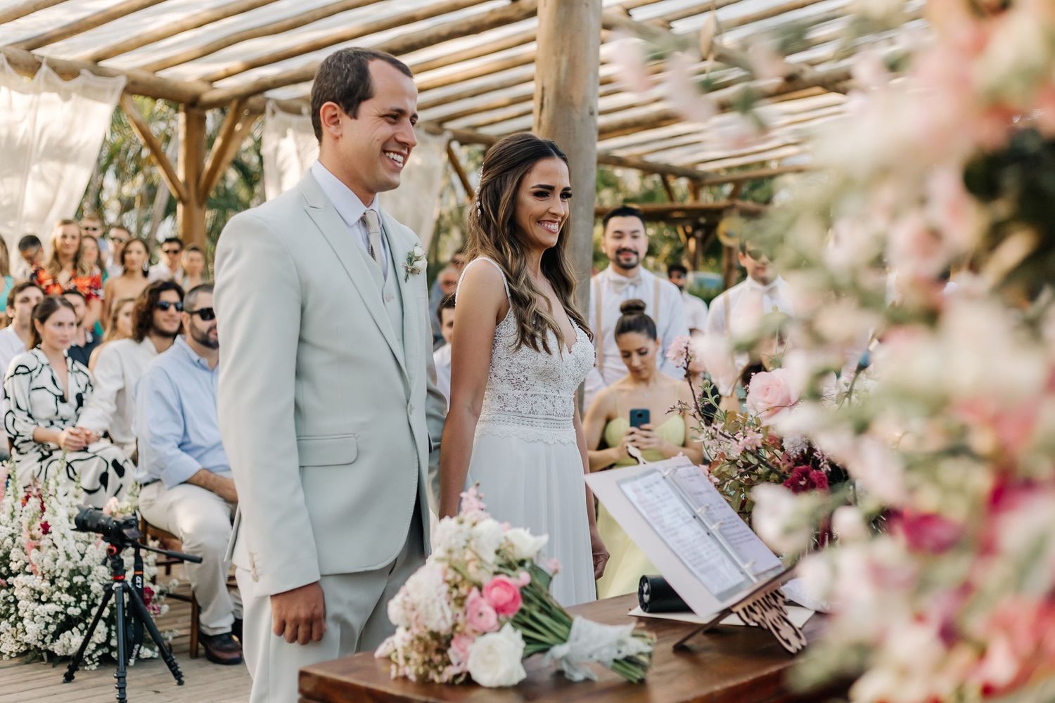 Wedding ceremony at rustic outdoor venue with wooden pergola and floral decorations.