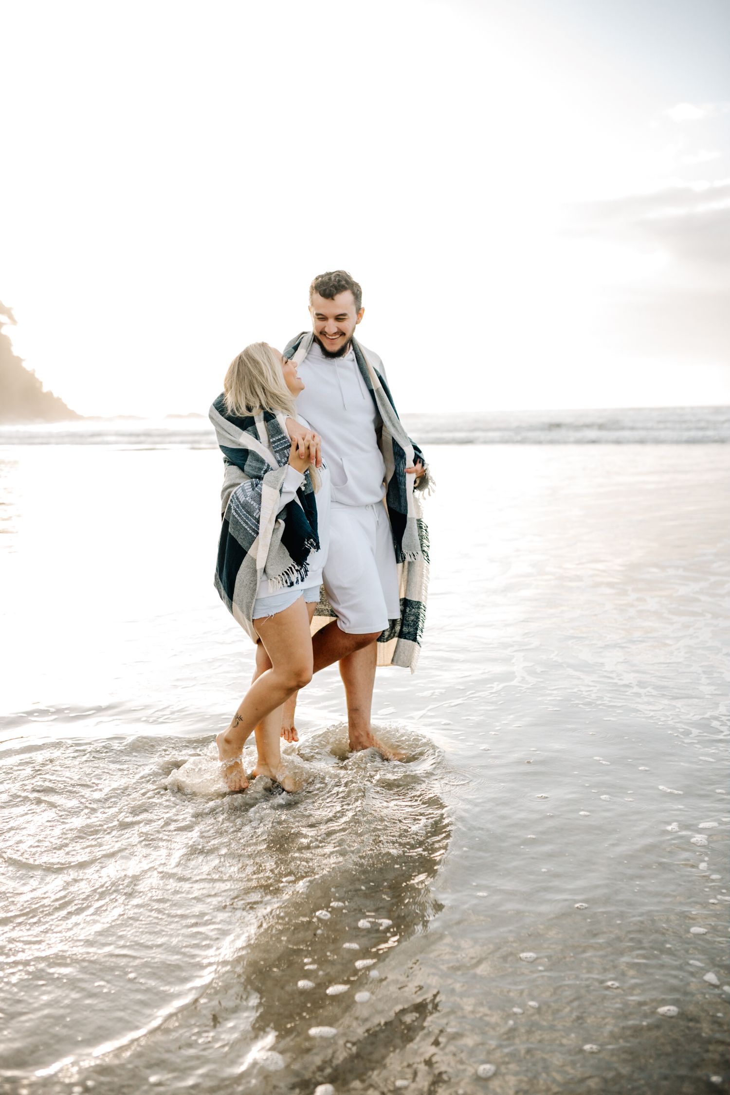 Two people splash and play in the shallow ocean waves during sunset.